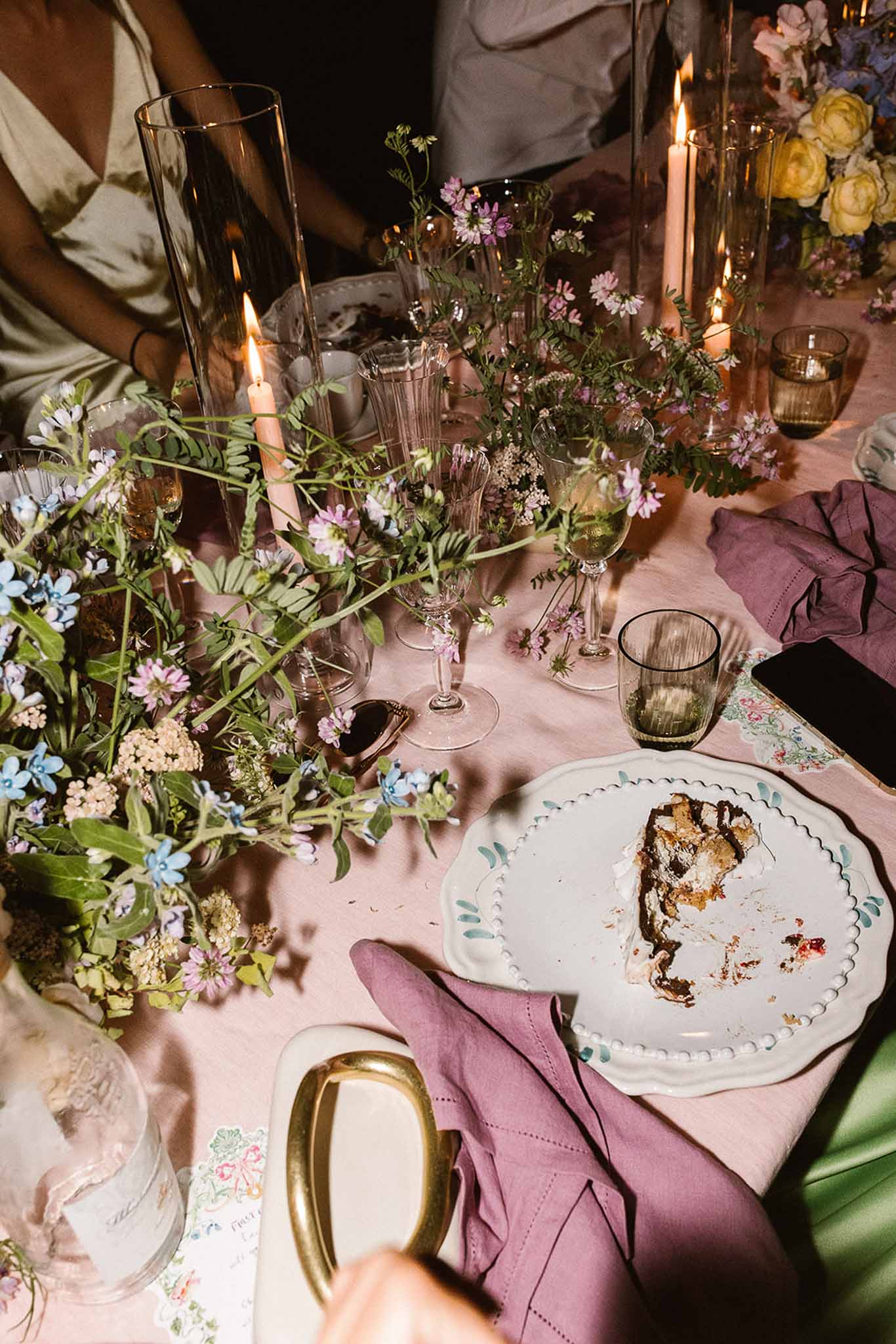Garden-party table with wildflower arrangements, teal-leaf plates, and smoky glass goblets on blush linen
