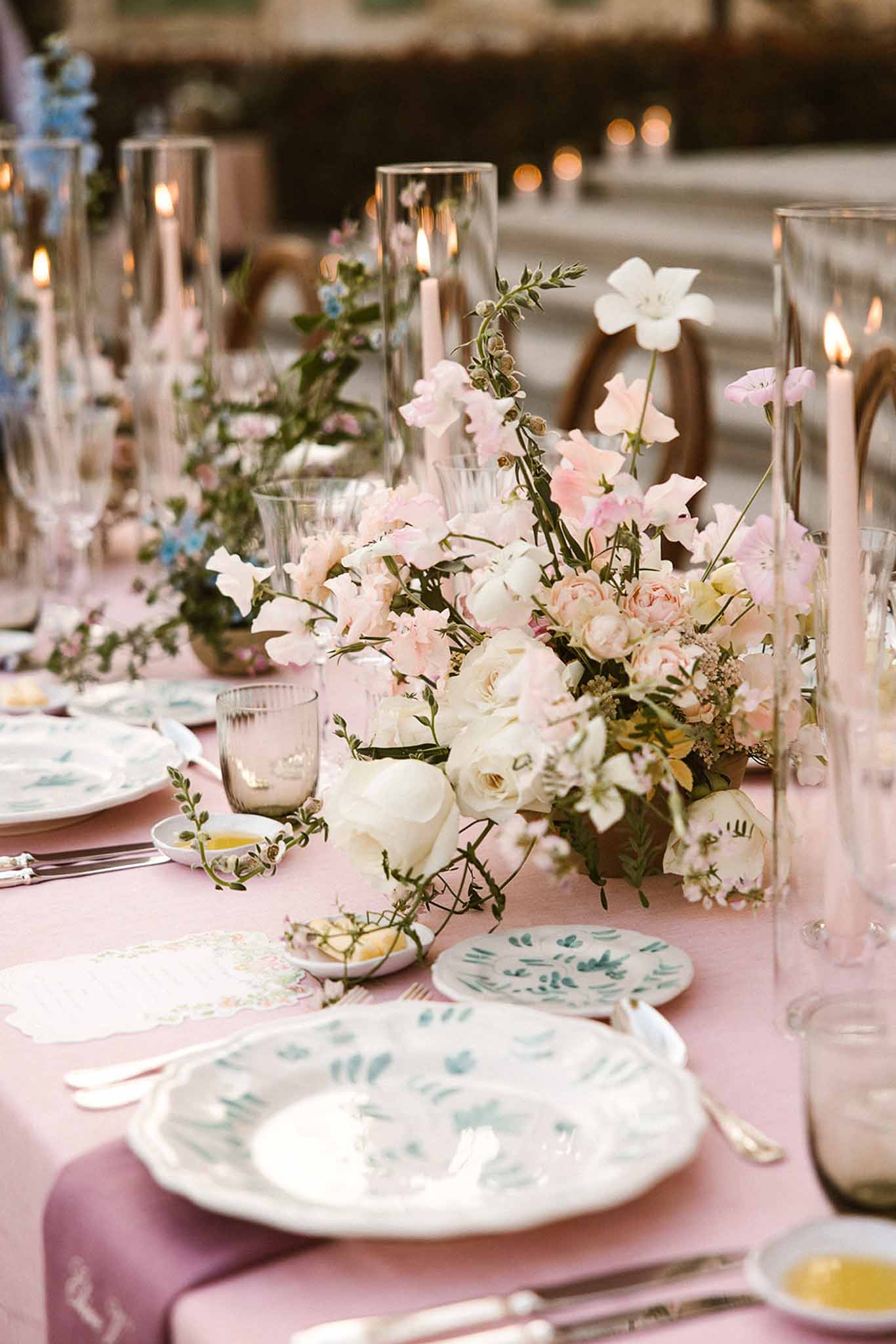 Outdoor reception tablescape with dusty pink linen, white peonies and blush roses, smoked-glass tumblers, and pink champag...