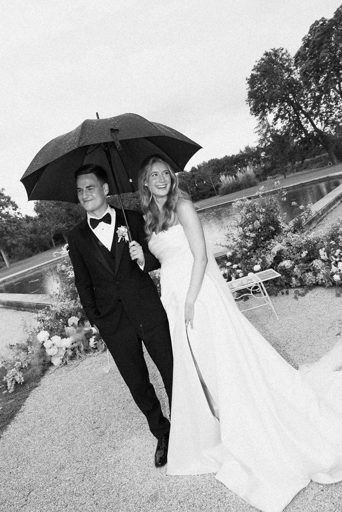 Black and white photo of bride and groom walking hand in hand in a garden
