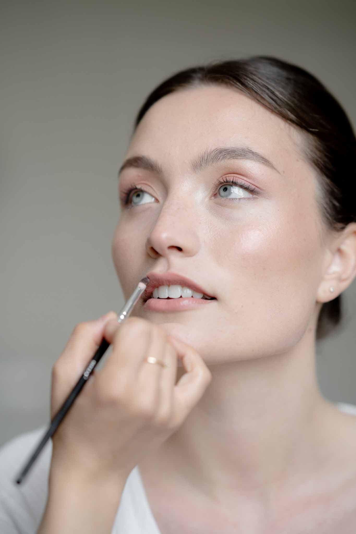 Makeup artist applying mauve lip color to bride with dewy skin and sleek updo