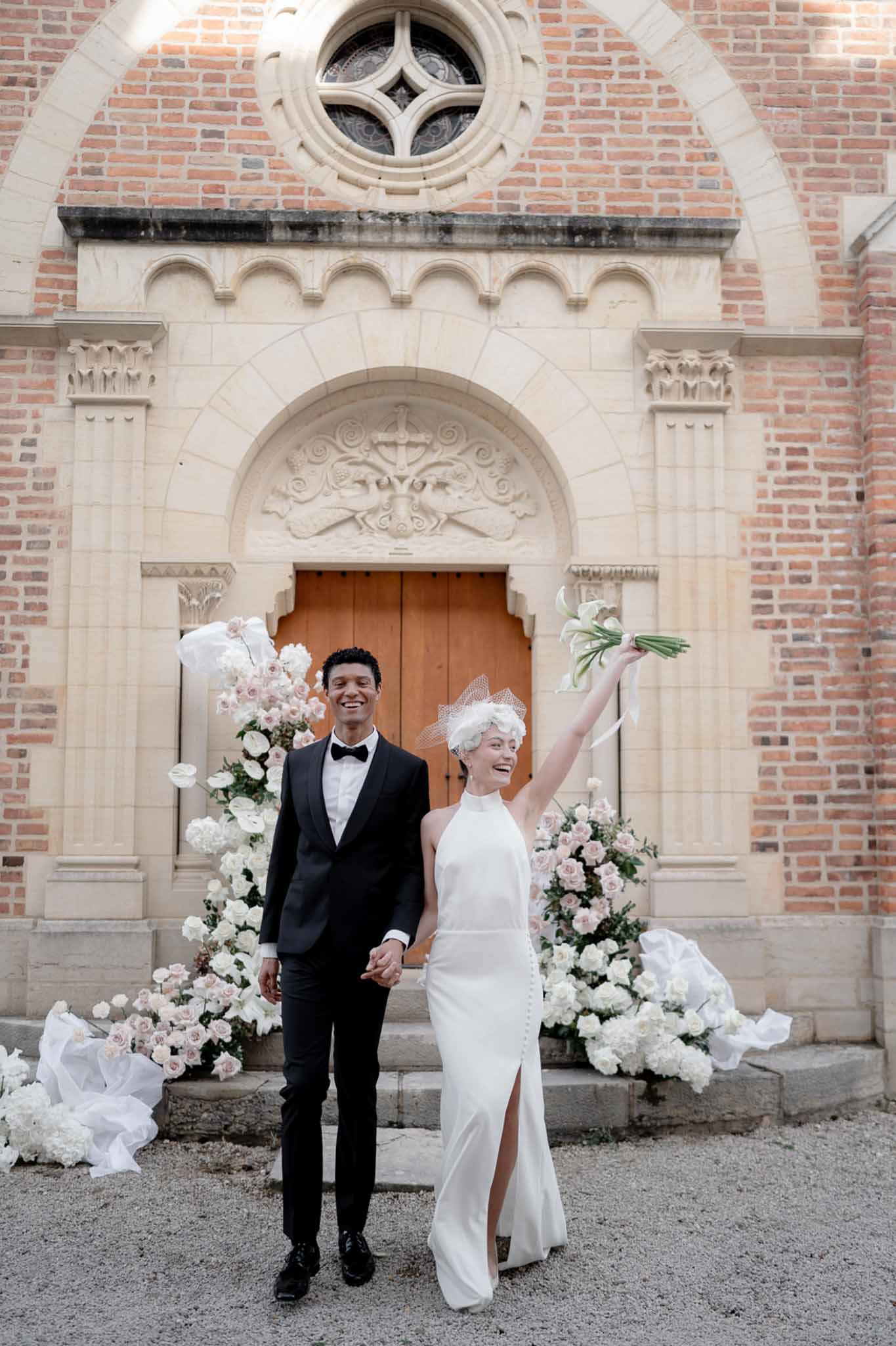 Couple exiting brick chapel with calla lily bouquet raised past white hydrangea staircase arrangements