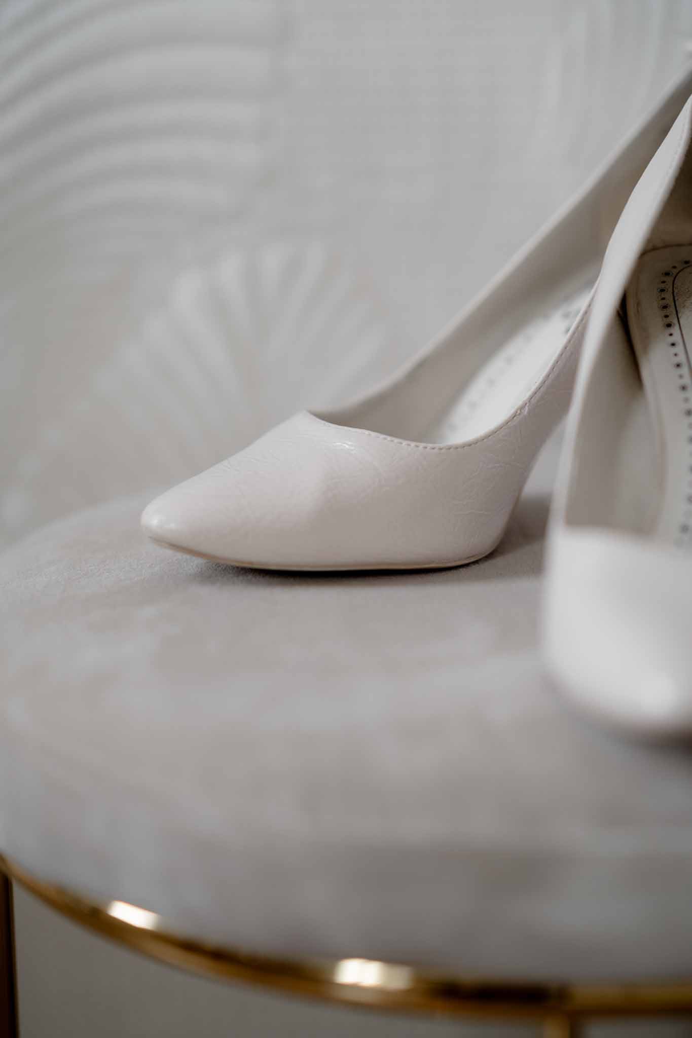 Close-up of ivory pointed-toe stiletto heels on cream embossed ottoman with gold trim base