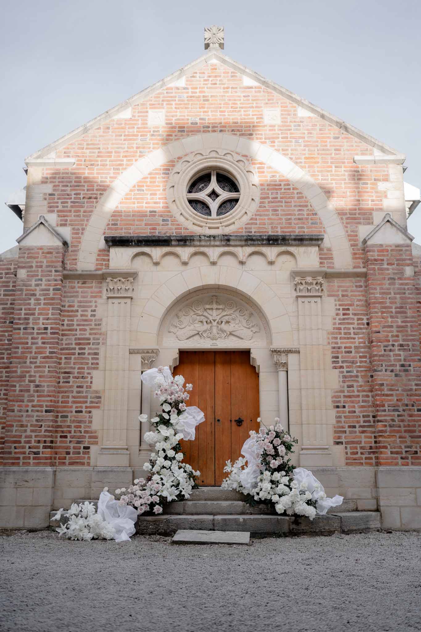 Red brick chapel entrance flanked by white rose and blush pink installations with billowing fabric