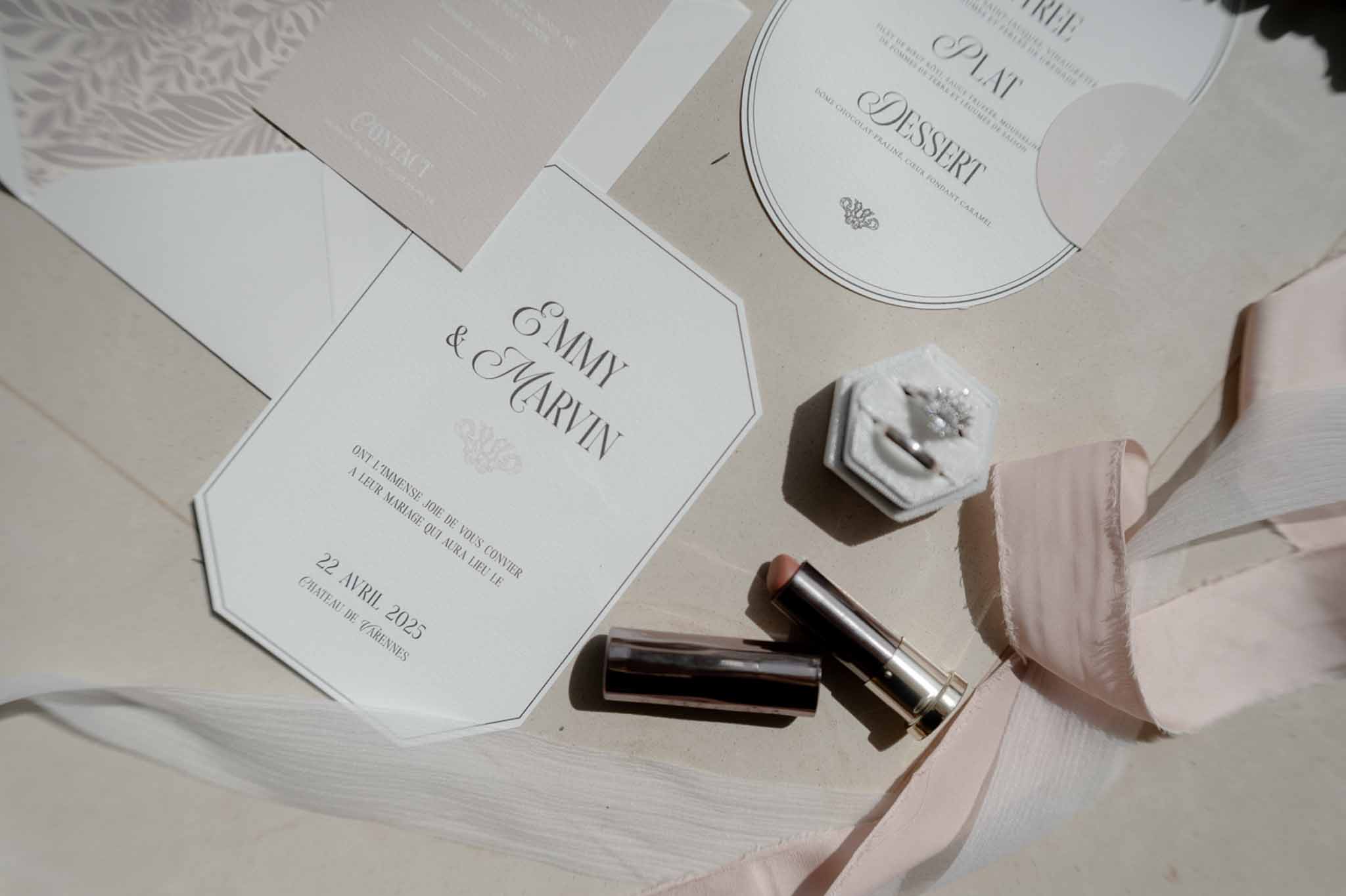 Octagonal ivory invitation with grey velvet ring box, nude lipstick, and blush silk ribbon on cream surface