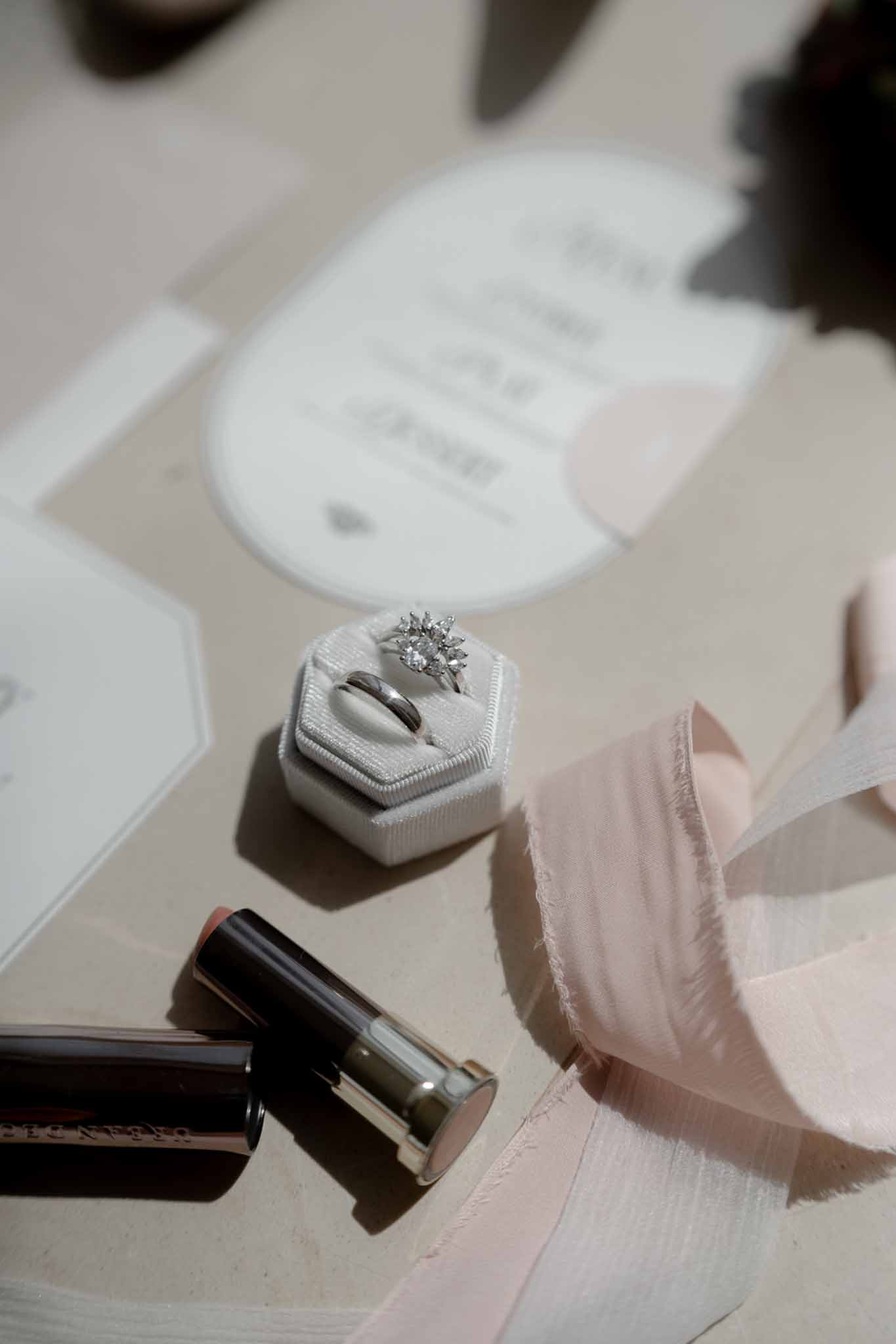 White hexagonal ring box with diamond starburst ring, blush silk ribbons, and die-cut stationery
