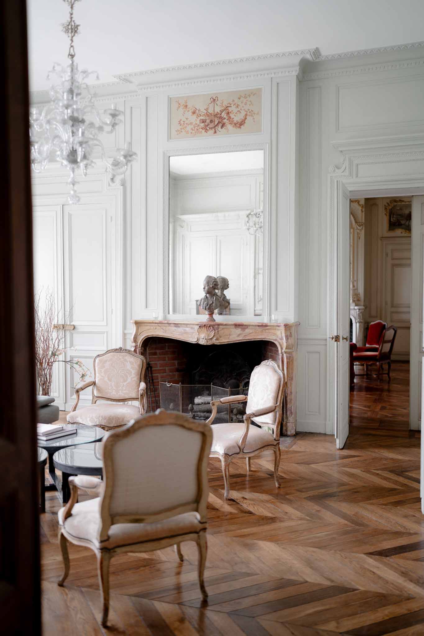 Grand chateau salon with boiserie panels, marble fireplace, crystal chandelier, and damask armchairs