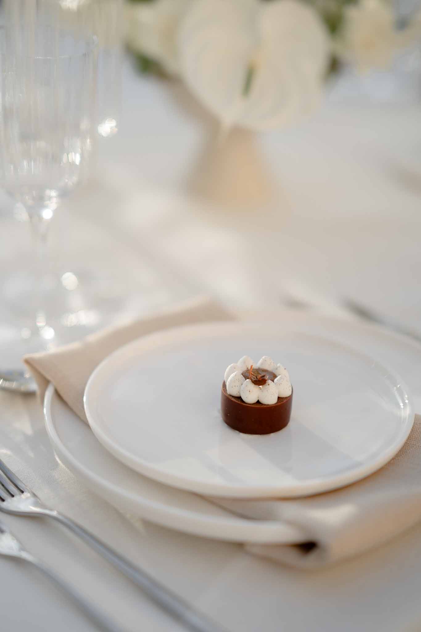 Miniature chocolate tart with cream rosettes on stacked white plates with crystal flute and white florals