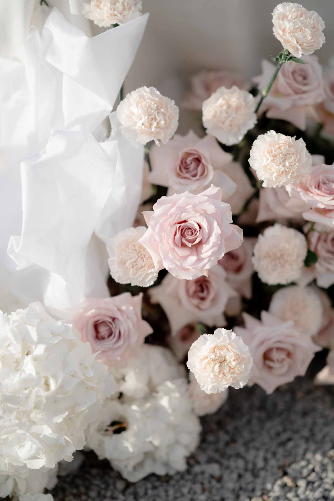 Close-up floral cluster of blush pink roses cream carnations and white hydrangeas on gravel with shallow focus