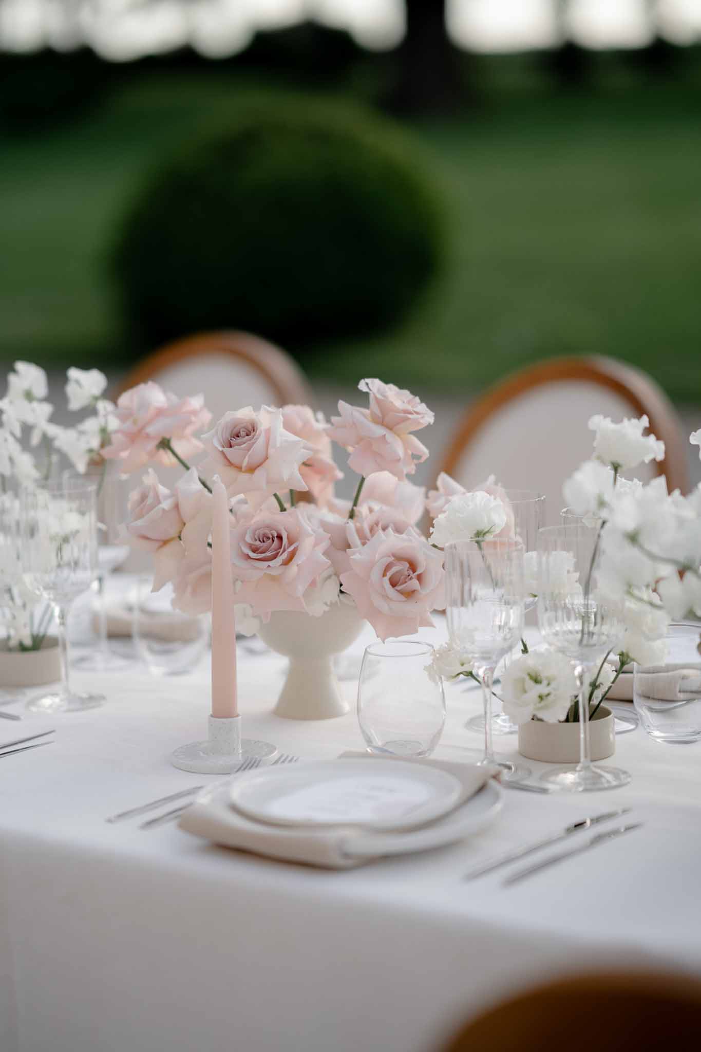 Blush rose and white sweet pea compote centerpiece with taper candle and bud vases on white outdoor reception table