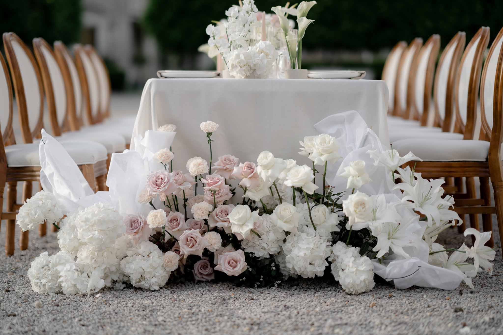 Ground-level white hydrangea and calla lily installation with organza ribbons at head table base