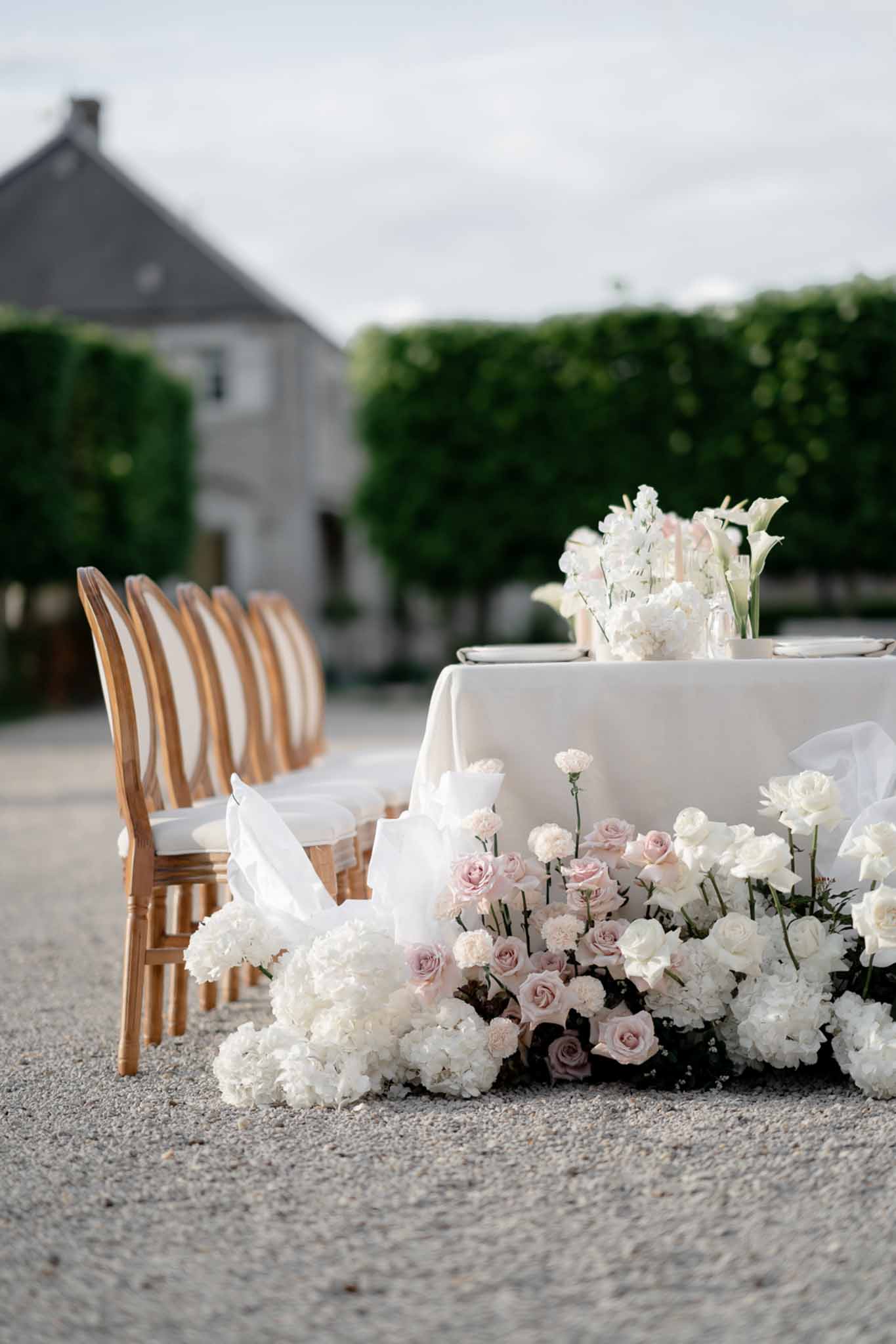 Sweetheart table with ground floral installation of white hydrangeas and blush roses on gravel