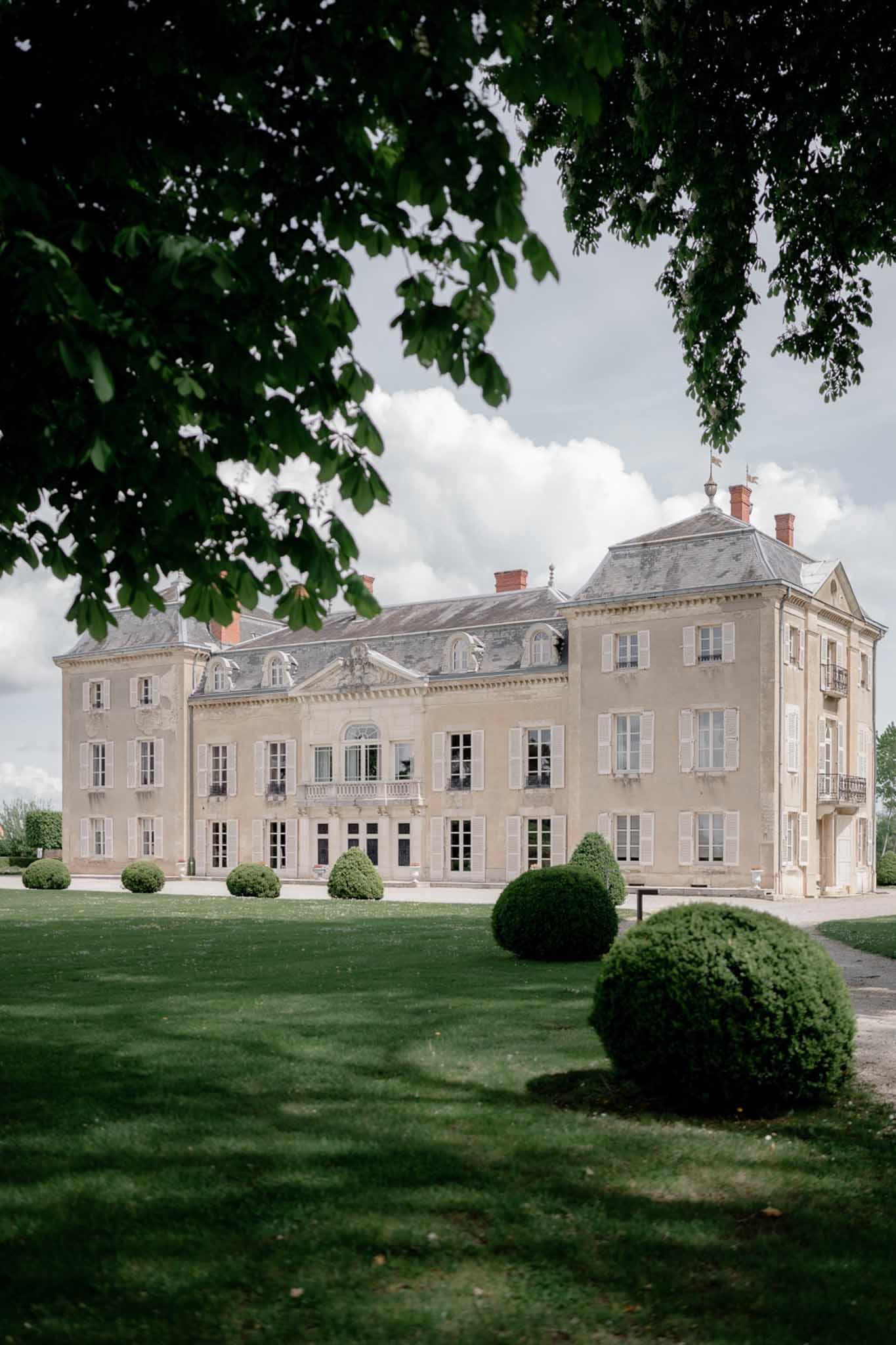 Symmetrical 18th-century French chateau in pale stone with mansard roof and topiary-lined lawn