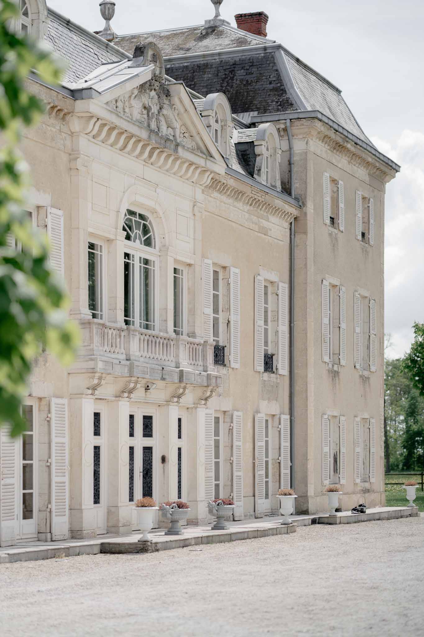 Cream stone French chateau exterior with white shutters mansard slate roof and gravel courtyard