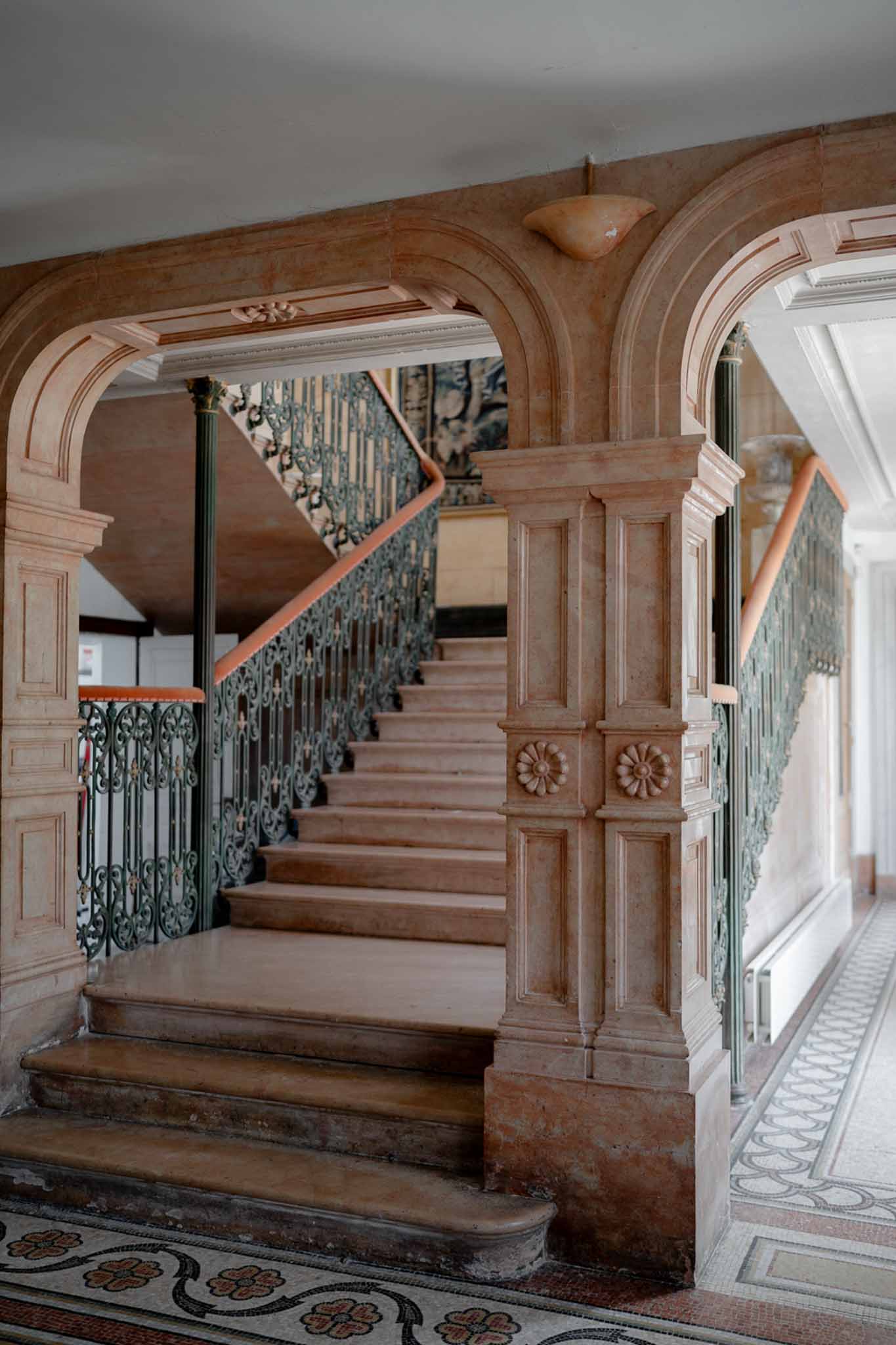 Grand chateau staircase with rose-toned marble green wrought-iron scrollwork balustrade and mosaic tile floor