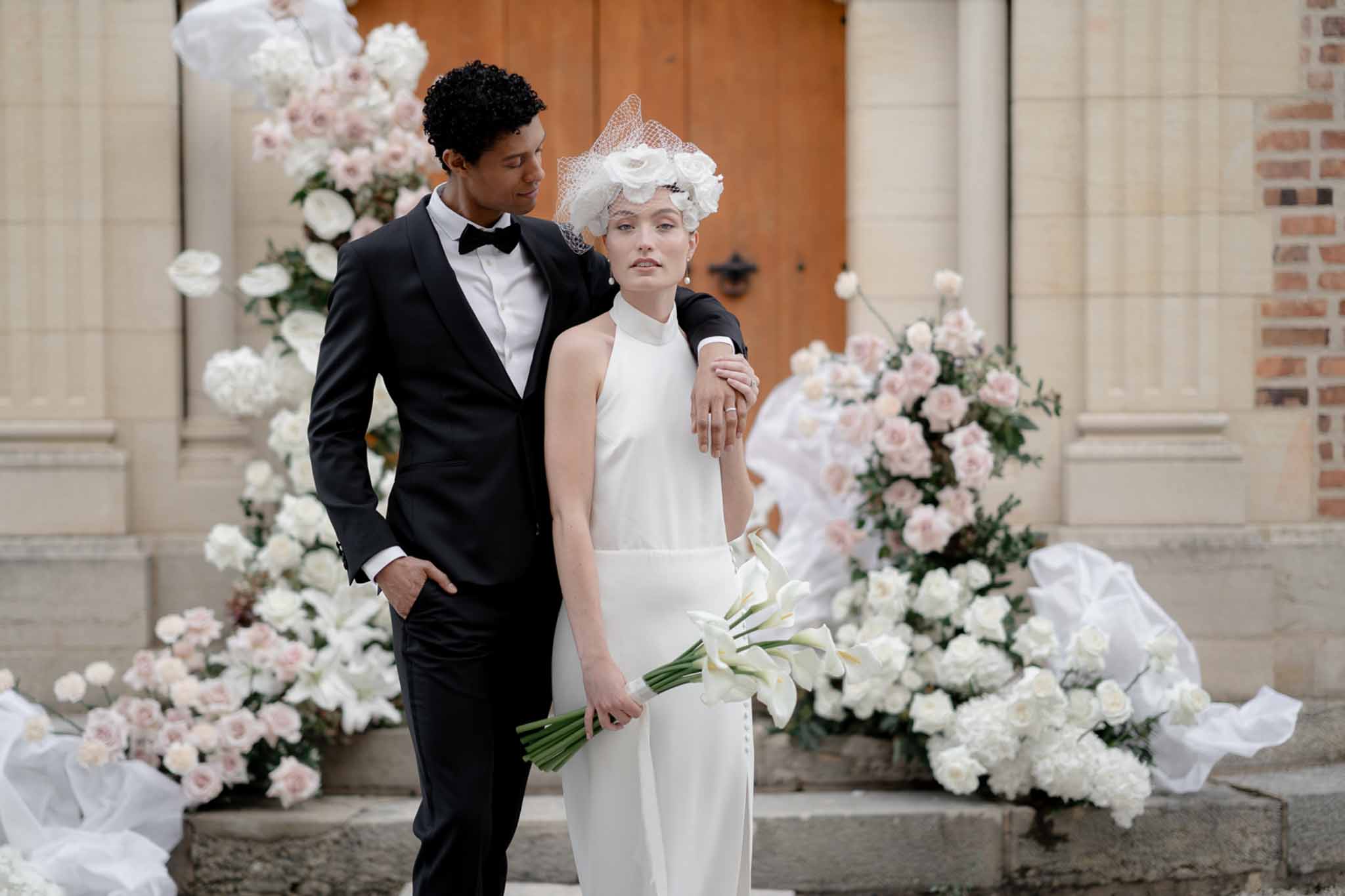 Bride and groom on church steps framed by cascading blush and white rose floral arch installation