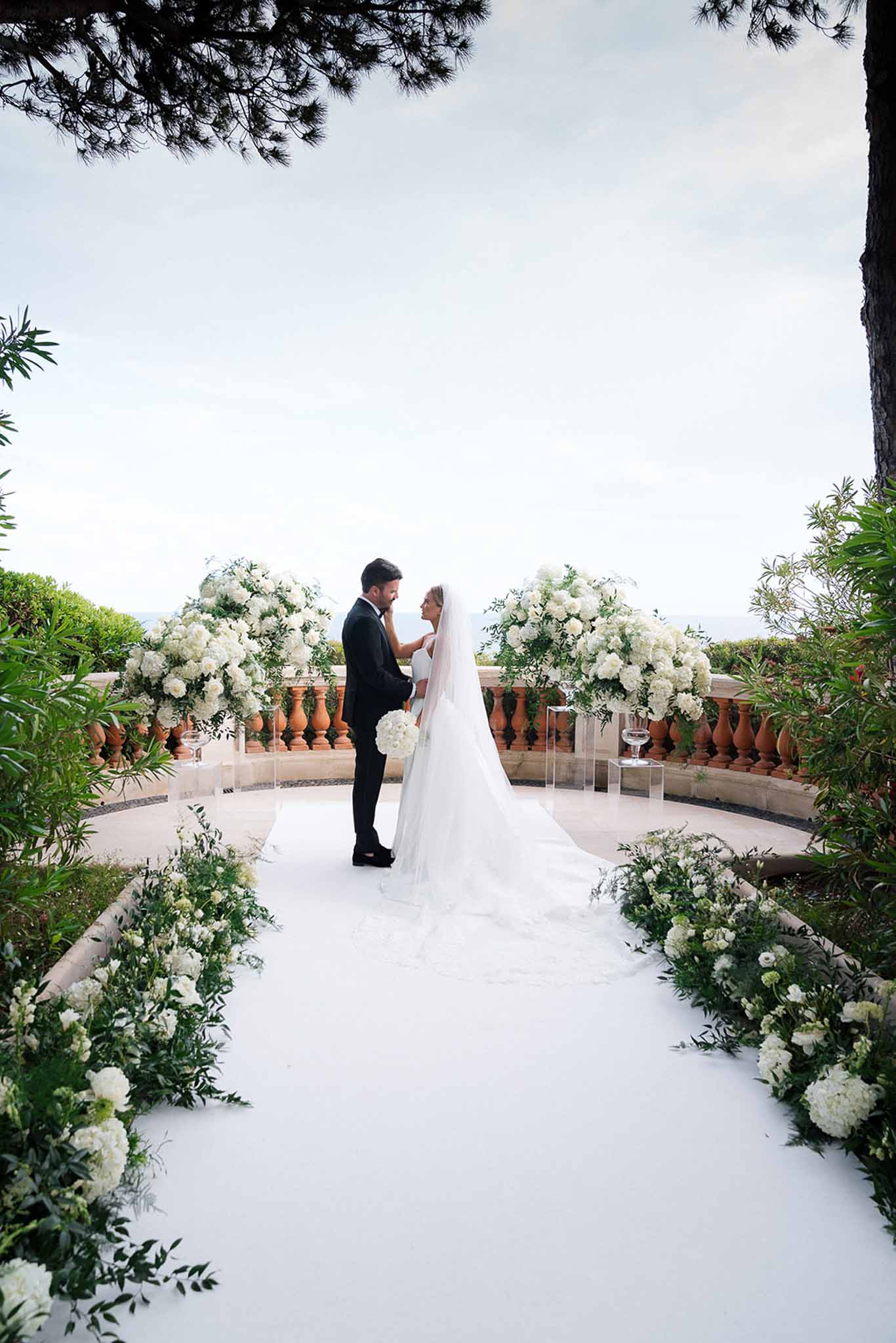 Bride with cathedral veil and groom at terrace altar with white hydrangea urns and sea view beyond