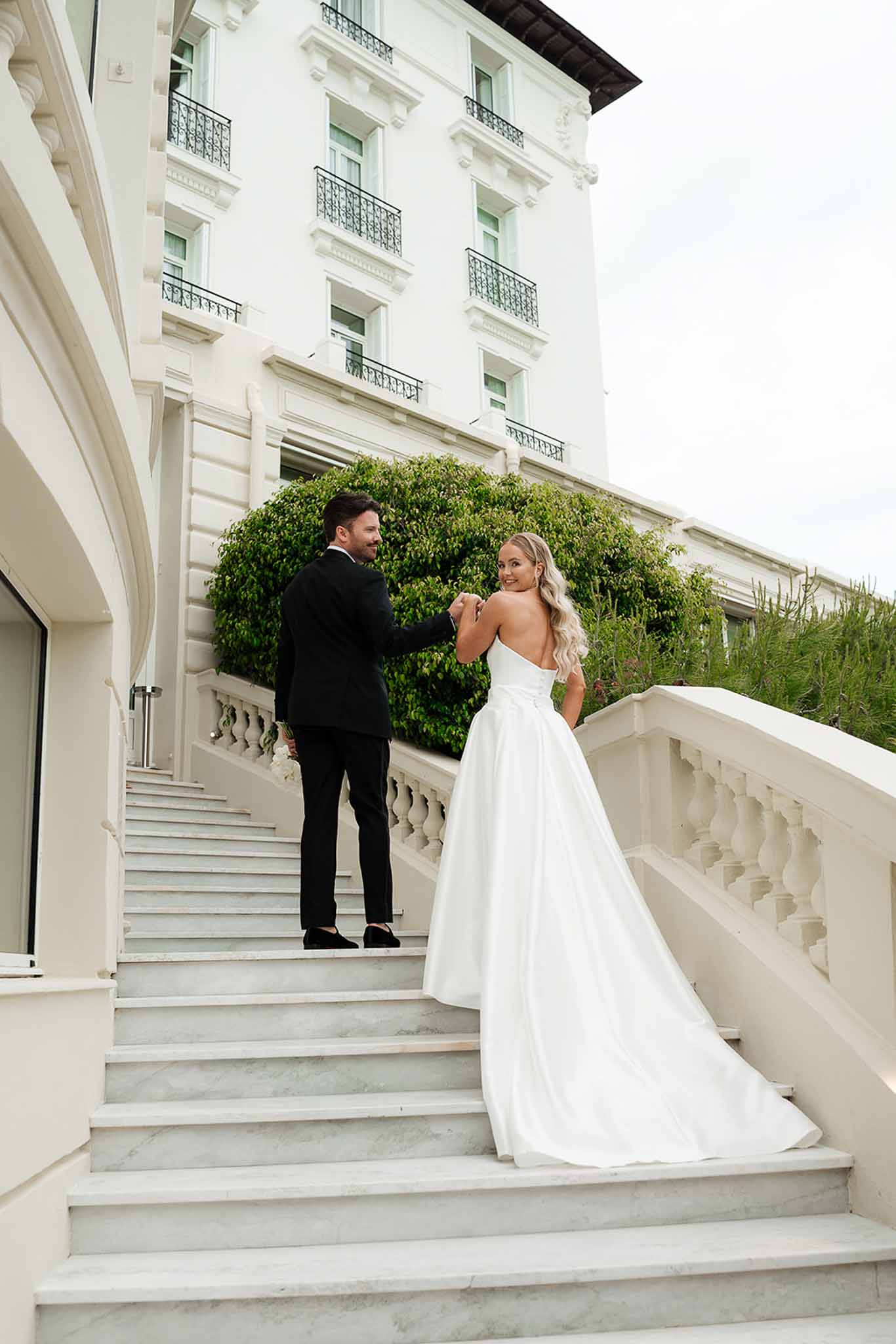 Couple on marble staircase of Belle Epoque hotel with wrought-iron balconies and white facade