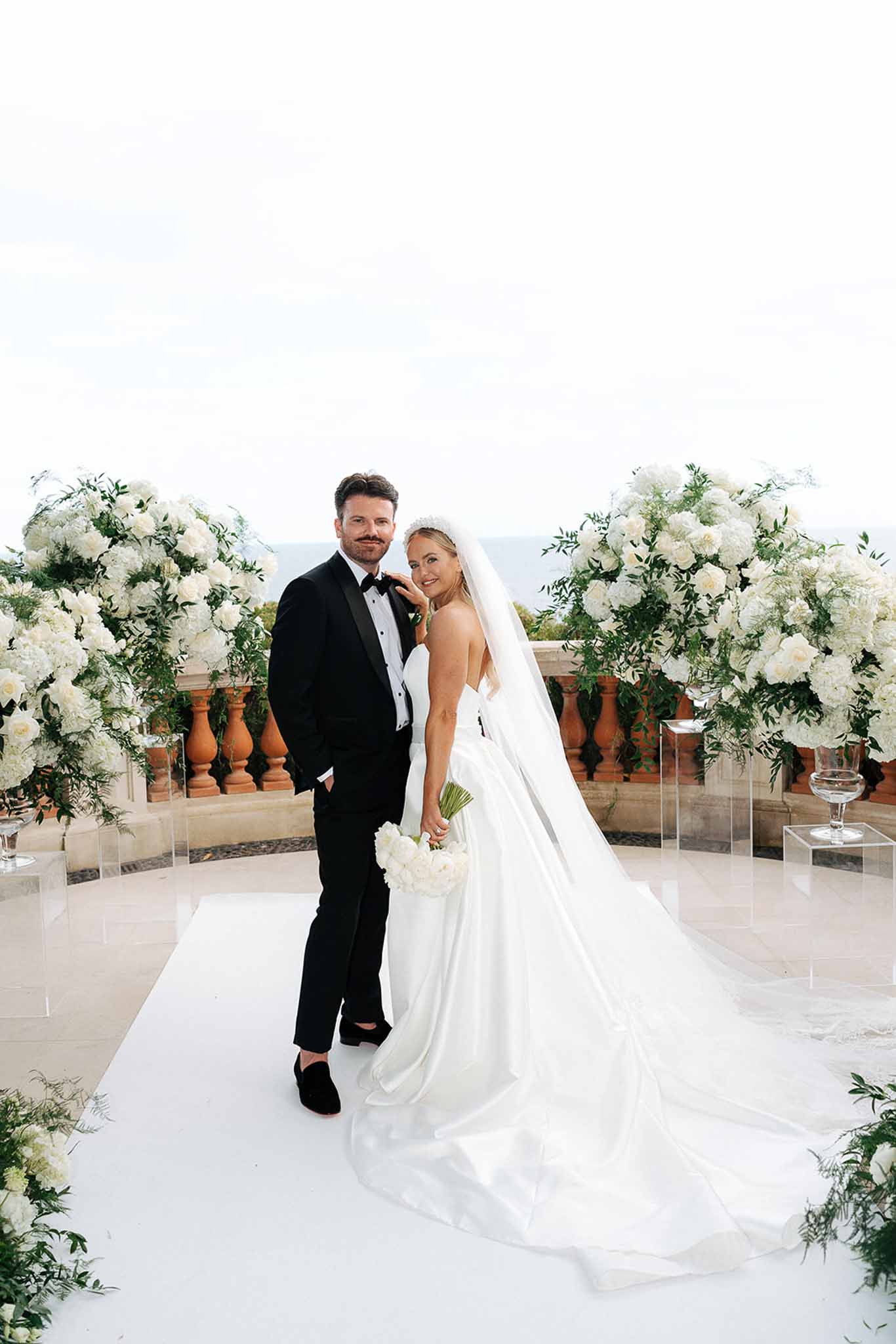 Bride and groom posing on a terrace ceremony aisle flanked by white peony installations in terracotta urns
