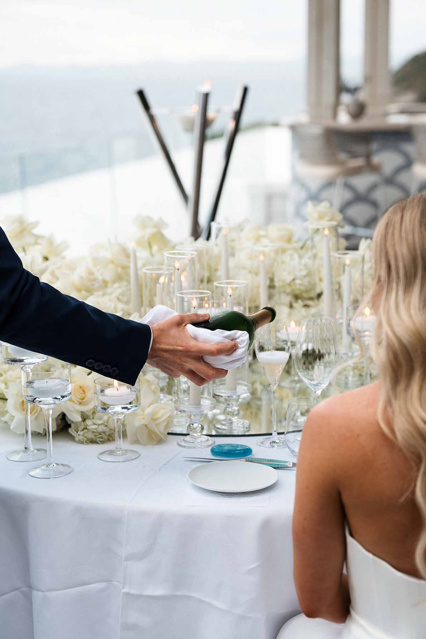 Waiter pouring champagne at head table with white rose and hydrangea runner and hurricane candle holders