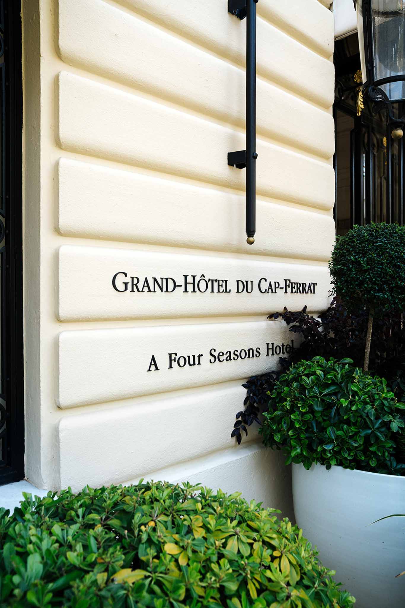 Grand-Hotel du Cap-Ferrat entrance sign in black serif on cream wall with boxwood topiary flanking