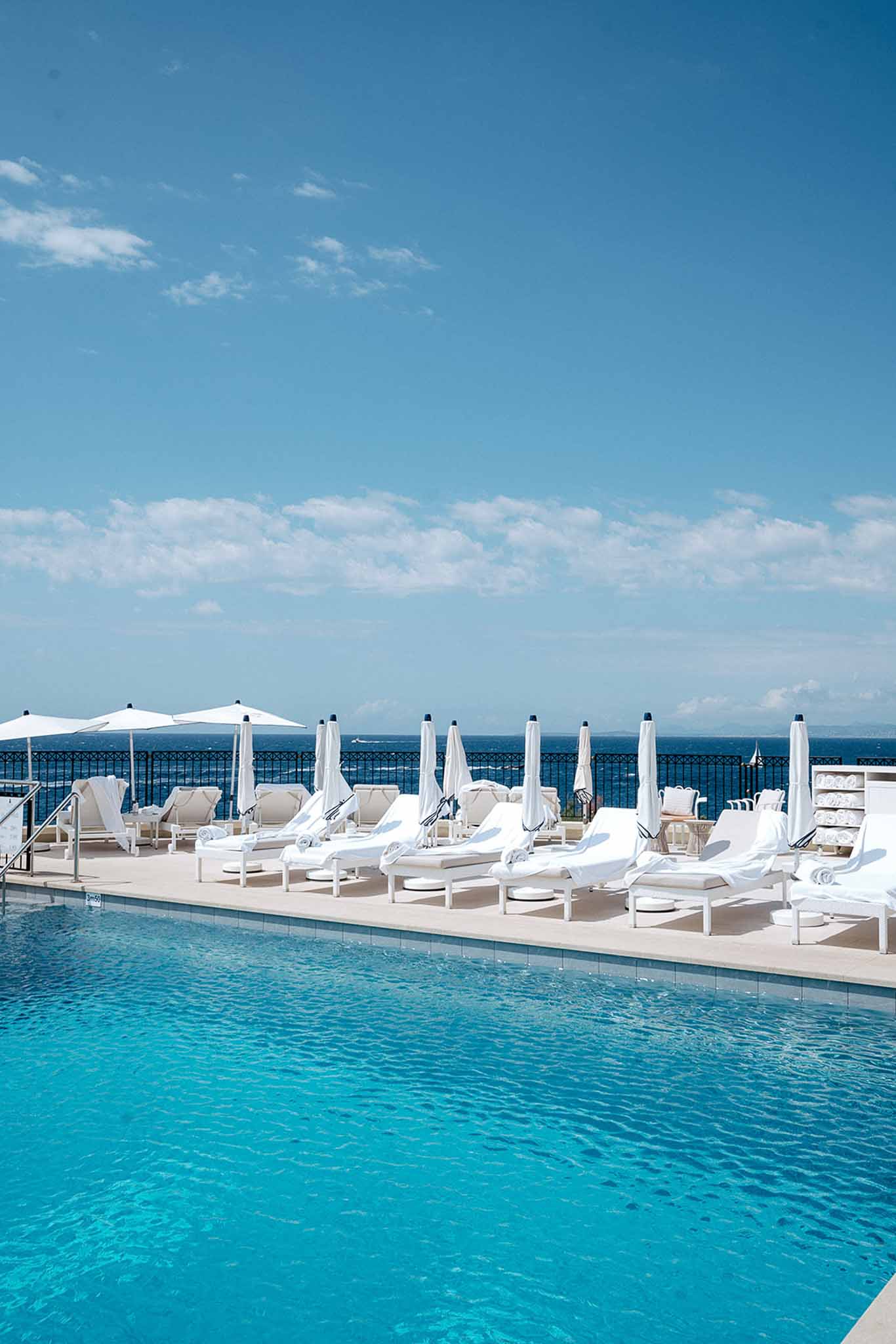 White sun loungers and parasols line a turquoise infinity pool terrace overlooking the sea at a coastal venue