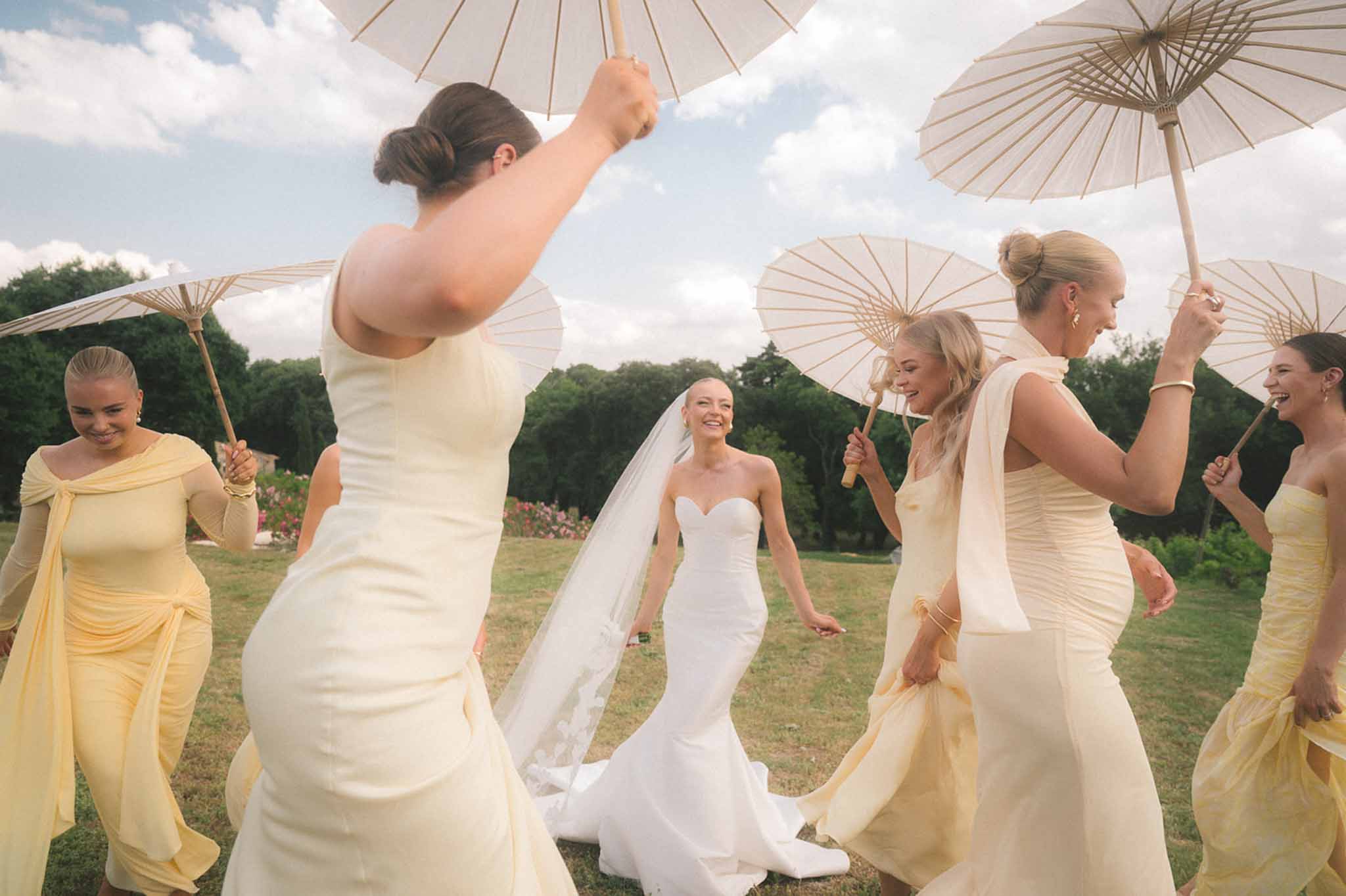 Bride in strapless mermaid gown with four bridesmaids in butter yellow dresses holding parasols