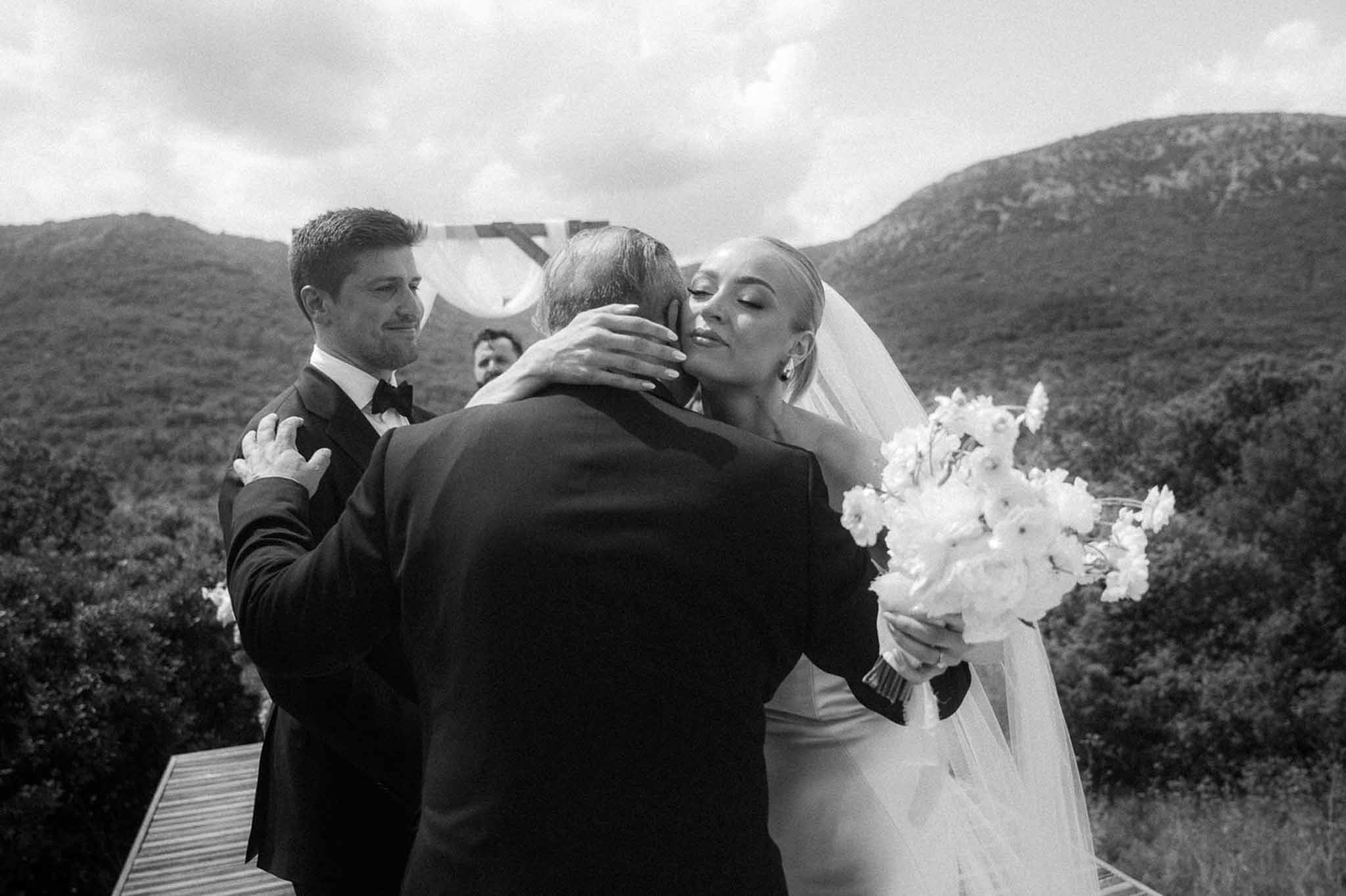 Black and white bride embracing father at altar as groom watches on elevated outdoor terrace
