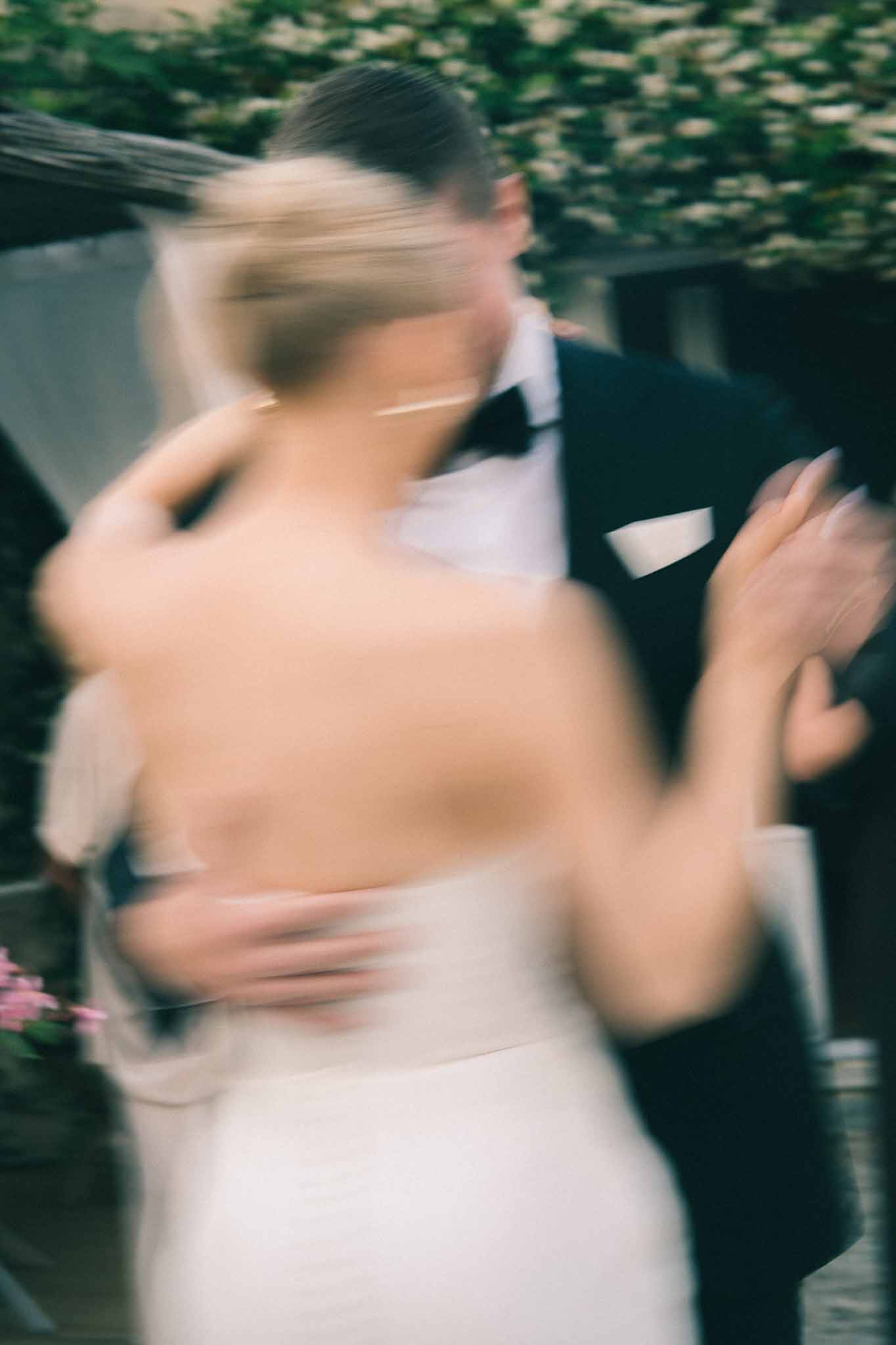 Motion-blurred portrait of bride and groom dancing outdoors, bride in backless white gown