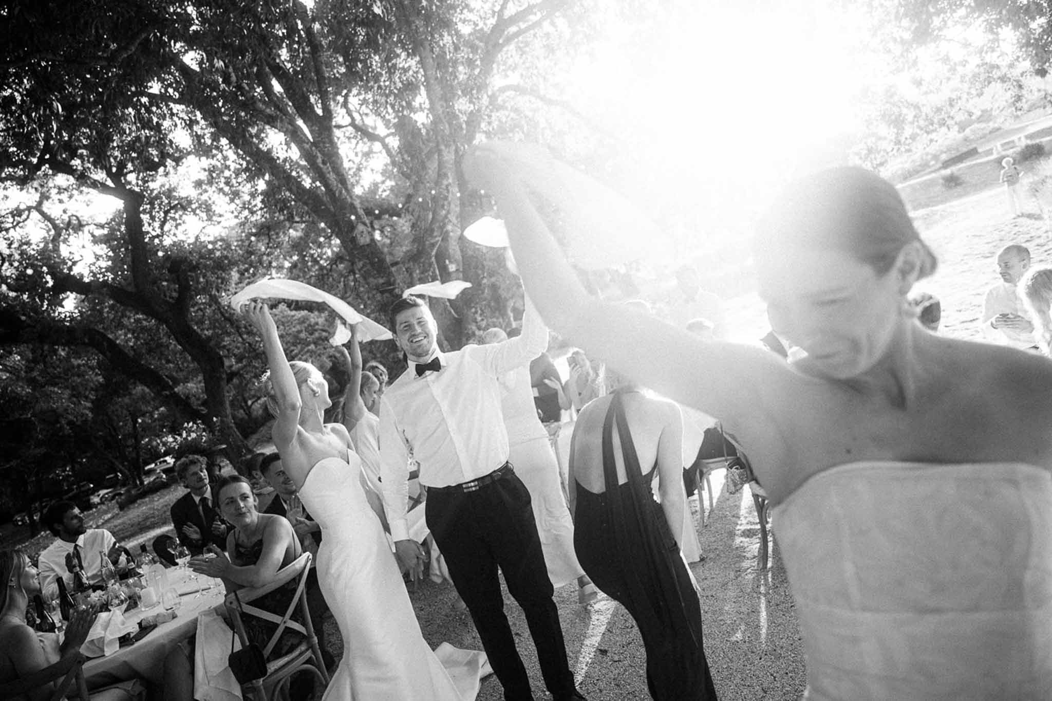 Black and white couple and guests waving napkins in traditional French celebration under courtyard trees