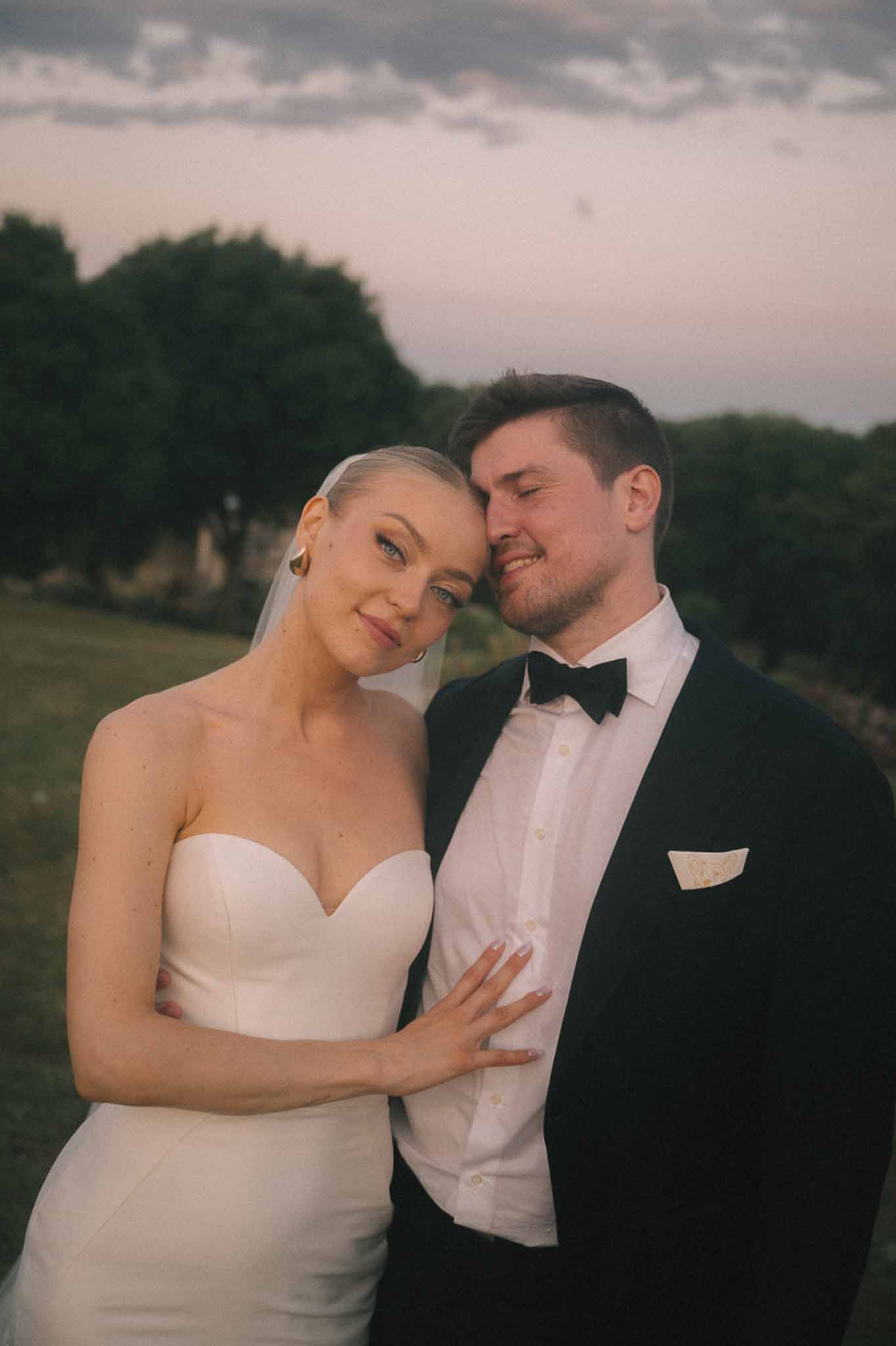 Close-up dusk portrait of bride in strapless gown with gold earrings resting hand on groom's chest