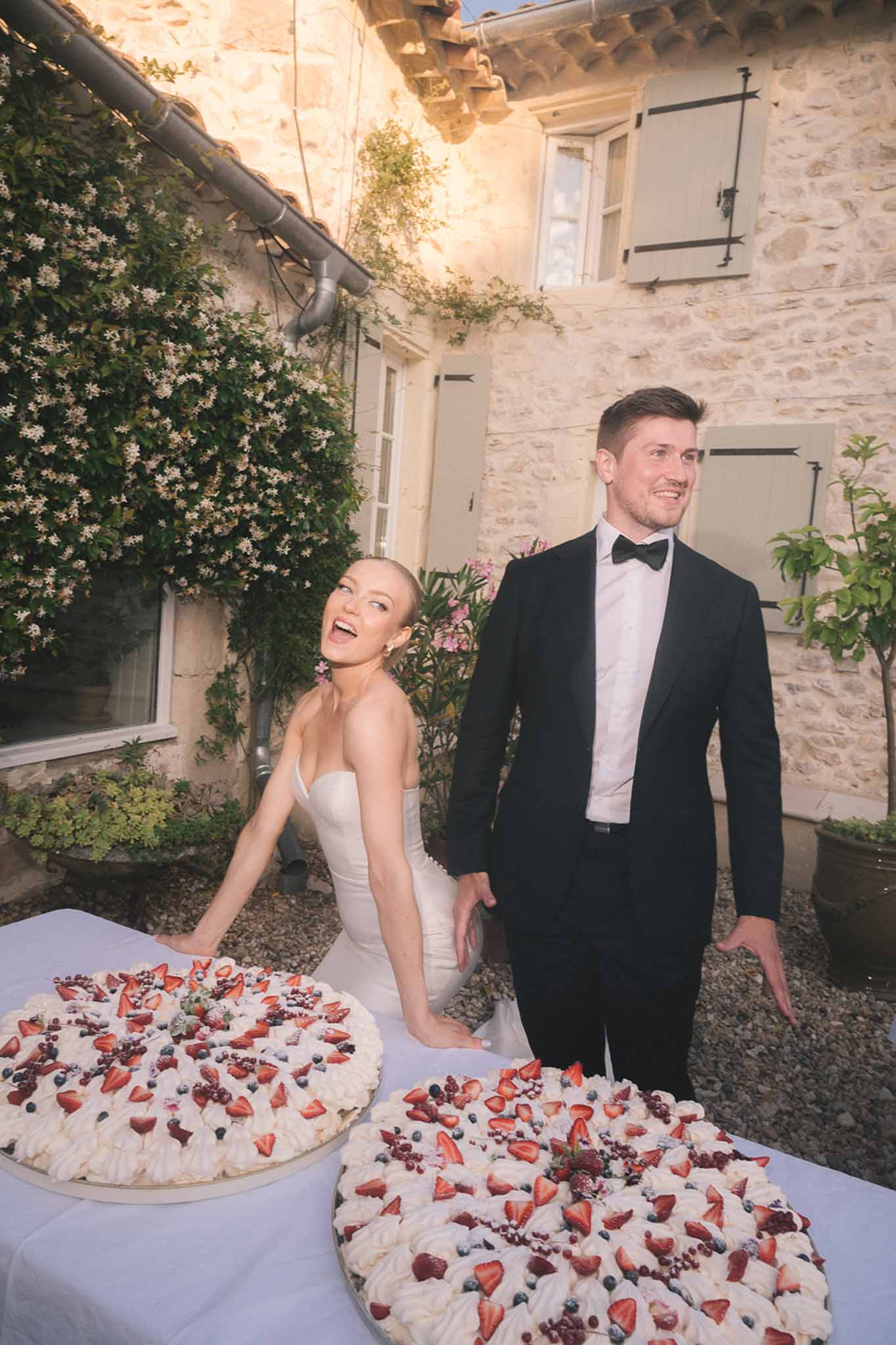 Couple laughing while cutting pavlova cakes with fresh strawberries at stone farmhouse courtyard