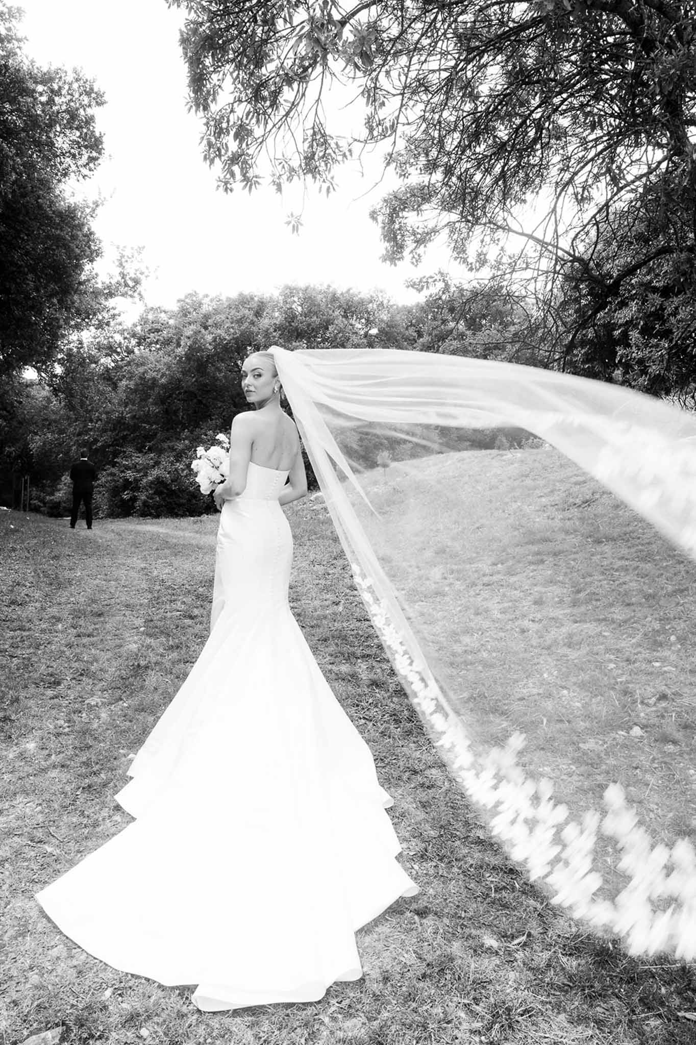 Black and white bridal portrait with cathedral veil billowing in wind on grassy hillside