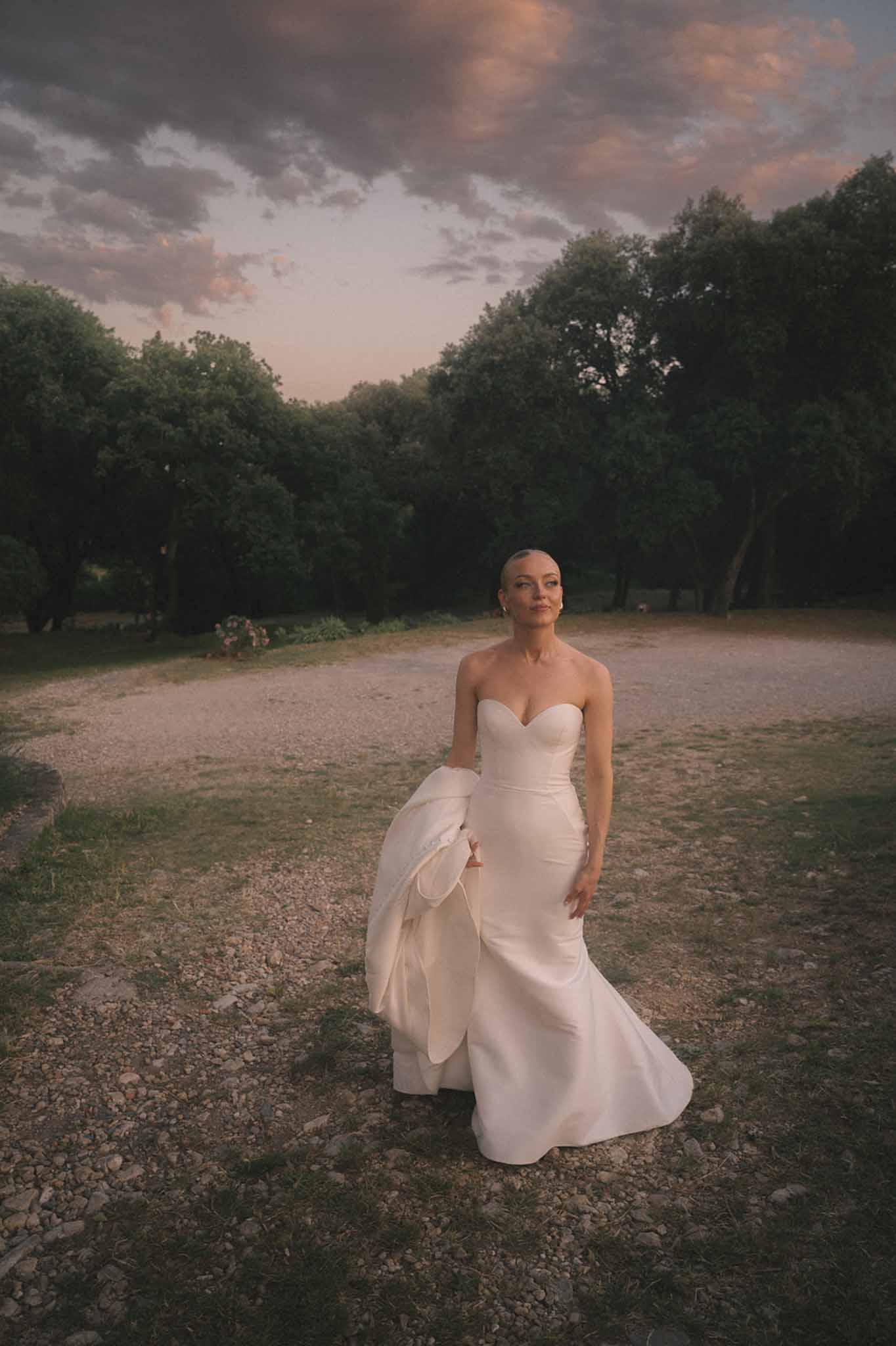 Bride in strapless ivory satin fit-and-flare gown with structured bow detail at sunset among mature trees