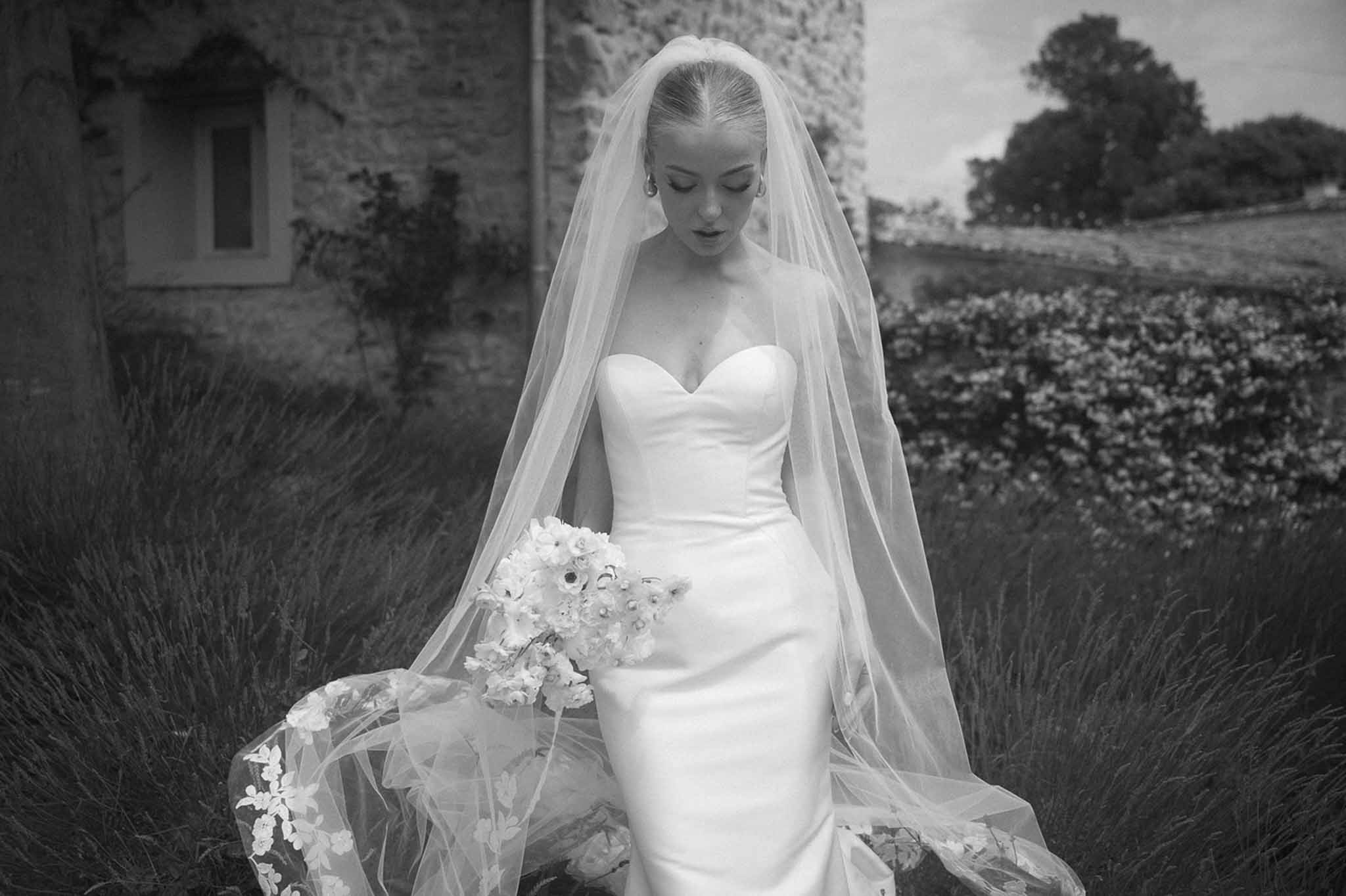 Black and white bride in strapless satin gown with lace-edged cathedral veil holding anemone bouquet