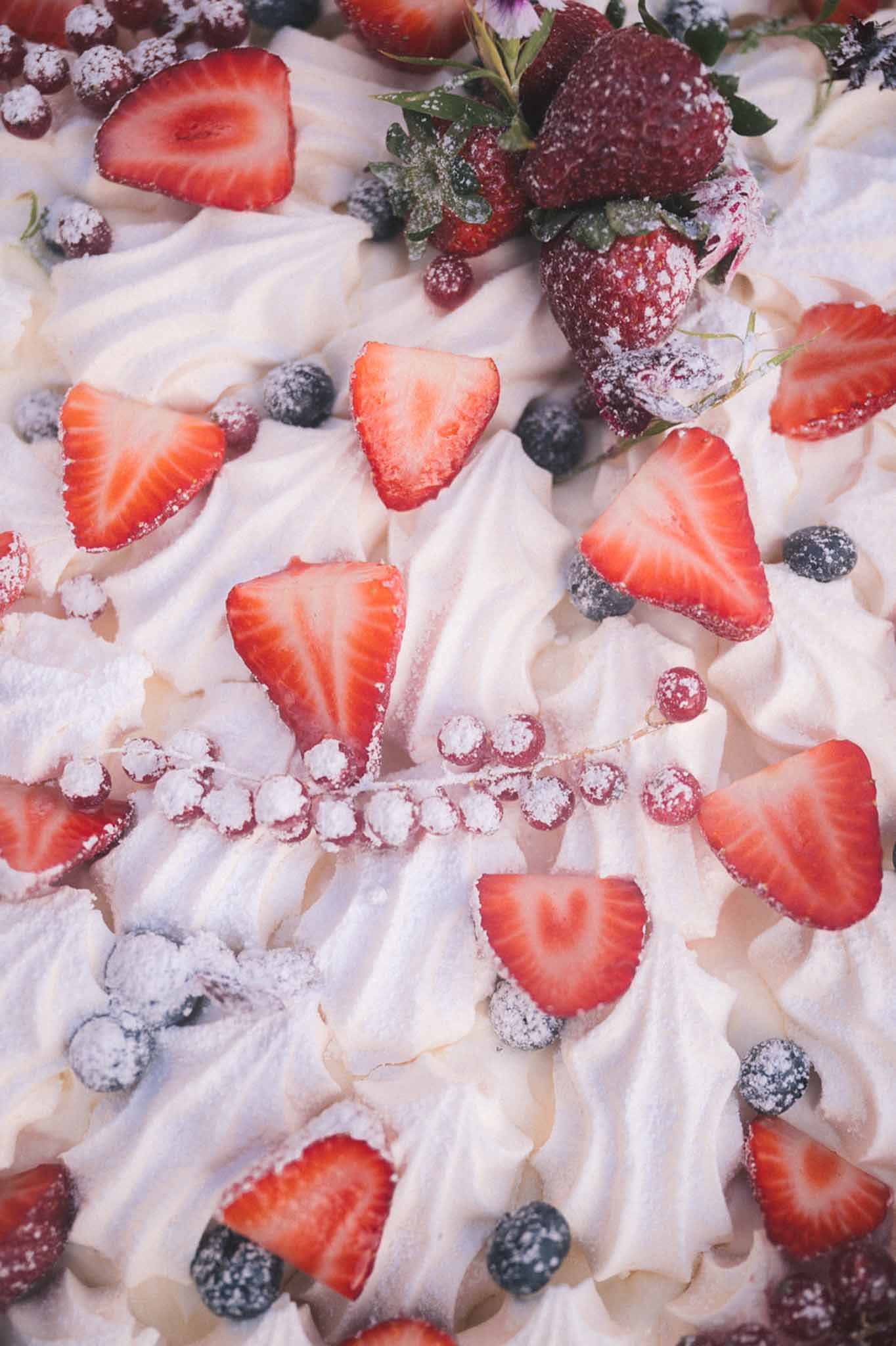 Close-up of meringue rosettes topped with sliced strawberries, blueberries, and red currants