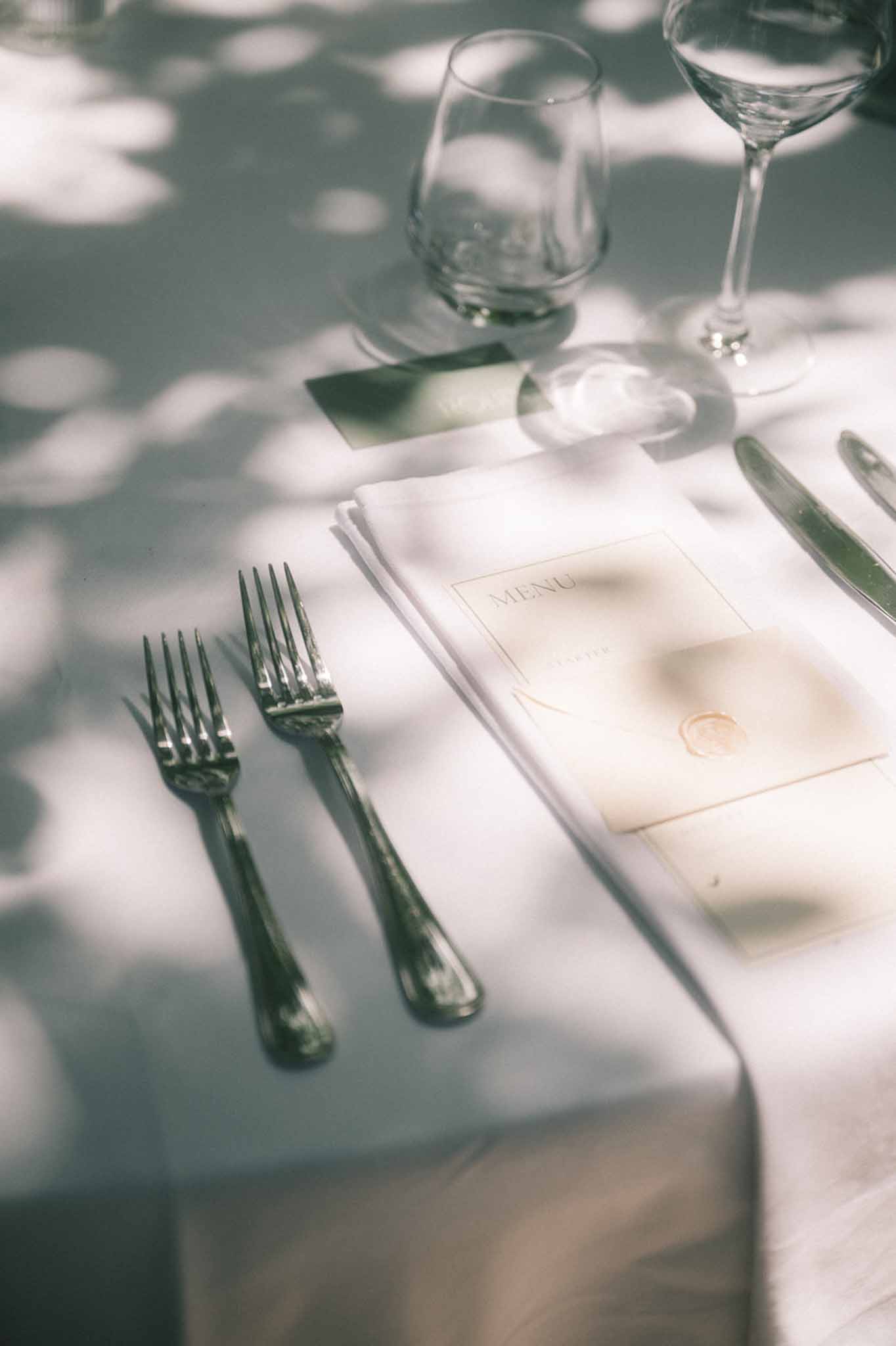 Wedding place setting with printed menu card sealed with gold wax seal on white linen napkin with crystal glassware