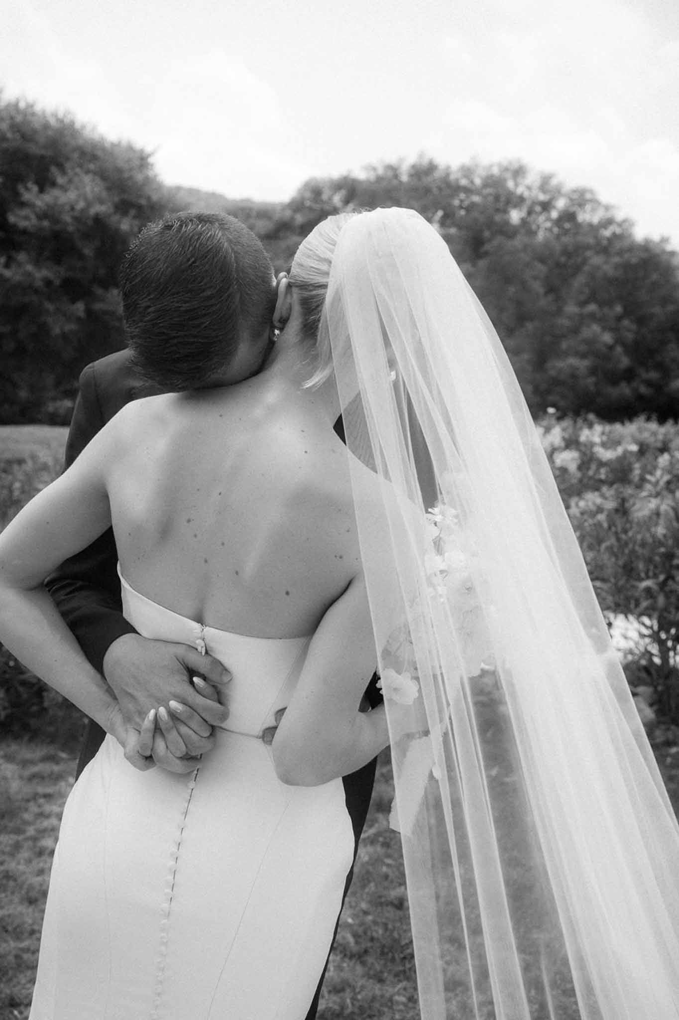 Black and white rear portrait of groom kissing bride's temple with applique-edged cathedral veil