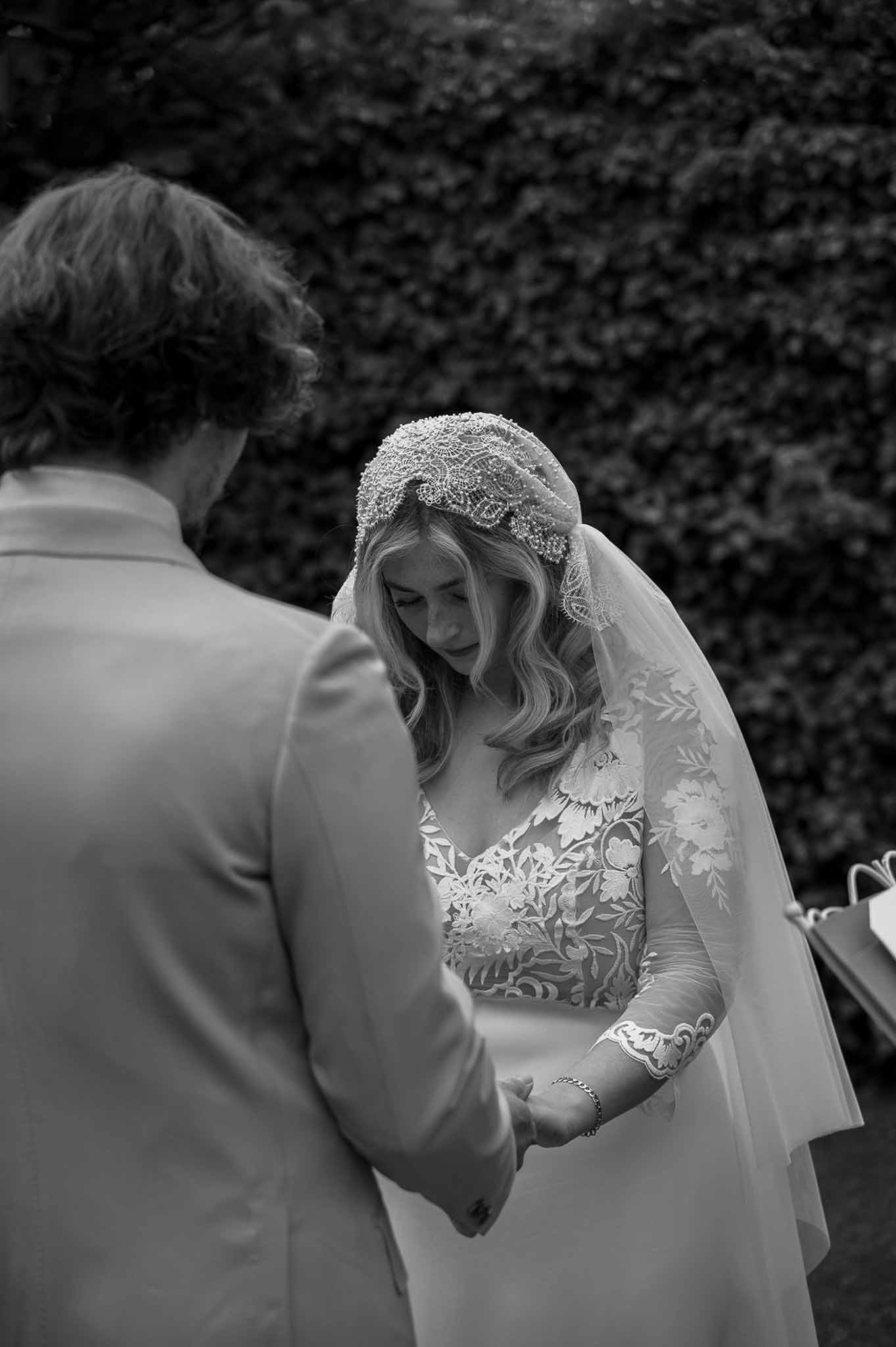 Black and white close-up of couple holding hands with beaded Juliet cap veil and lace sleeves