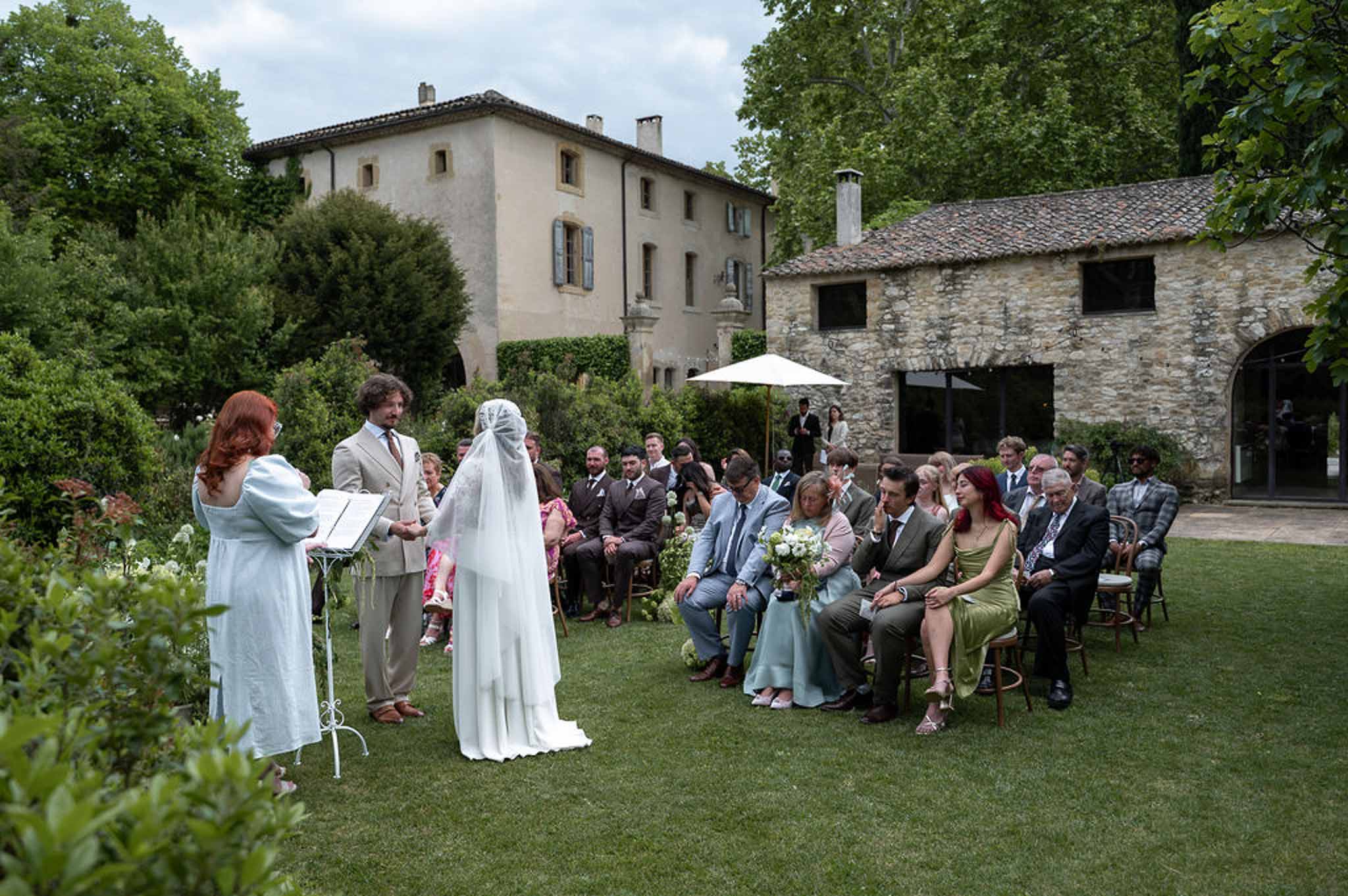 Outdoor lawn ceremony with bride groom and officiant before seated guests at French stone farmhouse