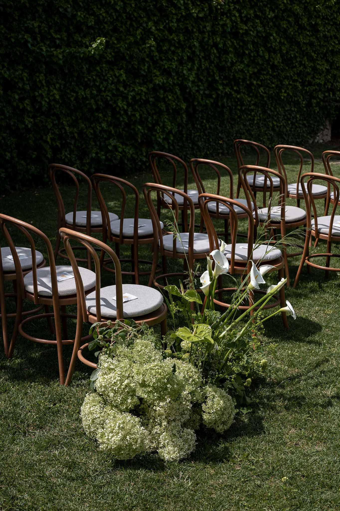 Outdoor ceremony setup with bentwood chairs and aisle floral arrangement of white calla lilies and hydrangeas