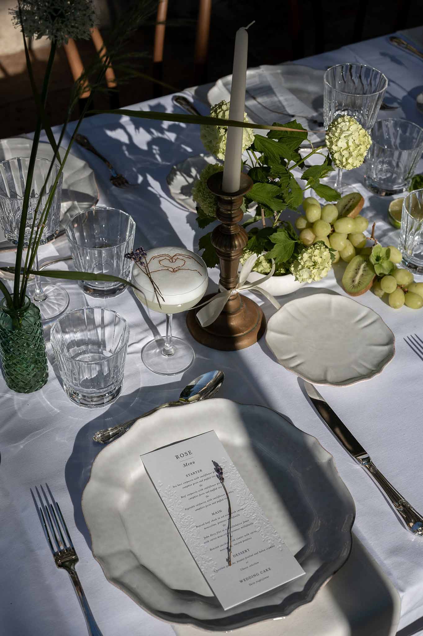 Scallop-edged plates with lavender menu card beside hydrangea centerpiece with grapes and brass candlestick