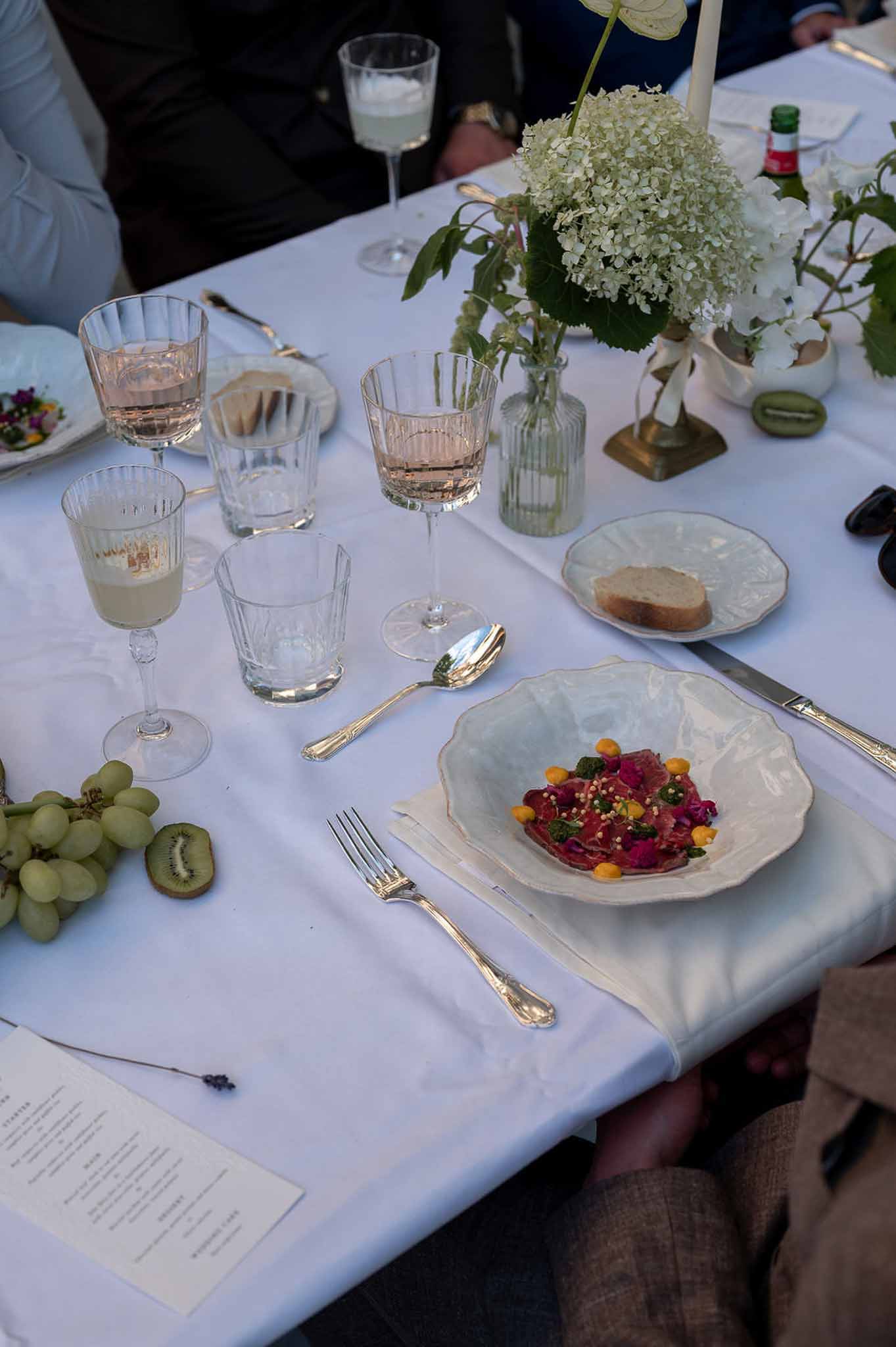 Place setting with ribbed blush and sage glassware, plated starter, grapes, and hydrangea bud vase