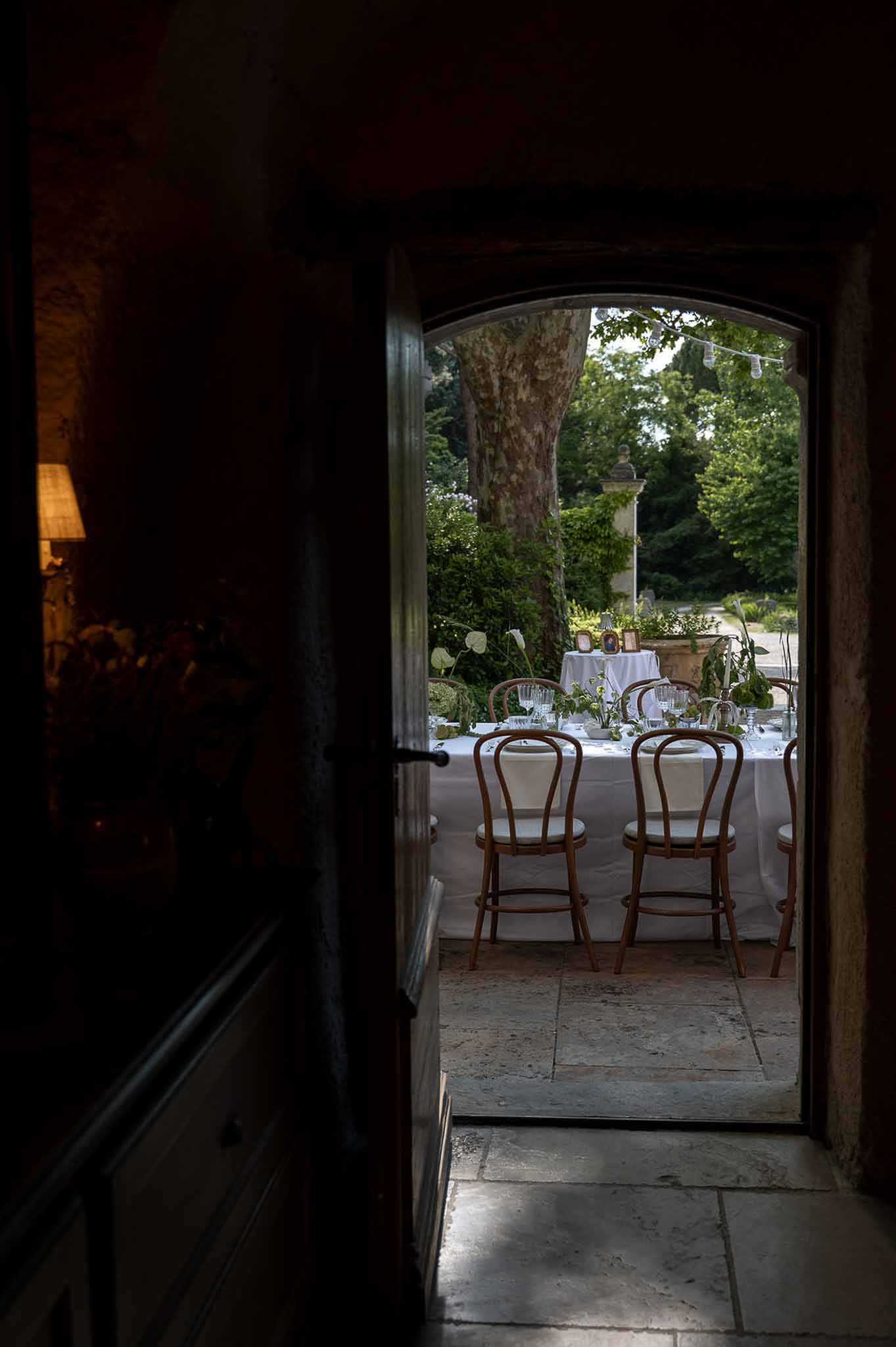 Reception table seen through dark arched doorway with calla lily greenery string lights and garden trees