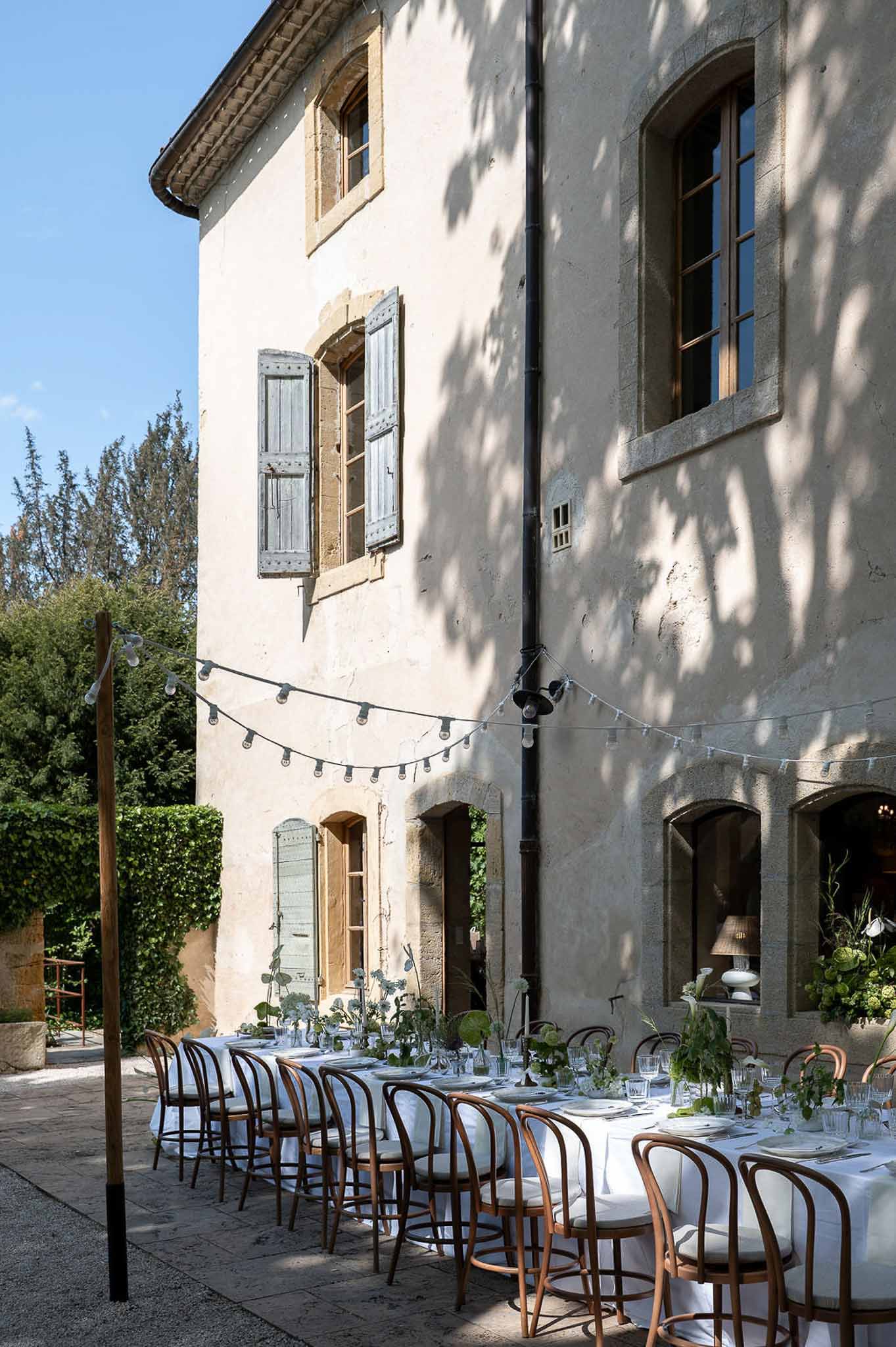 Courtyard banquet table with green botanical runner artichoke accents bentwood bistro chairs and globe string lights