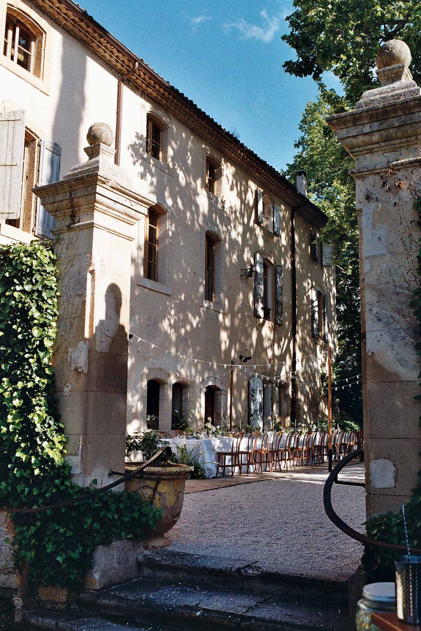 Ochre bastide courtyard with long banquet table, festoon lights, and stone gate pillars with ivy