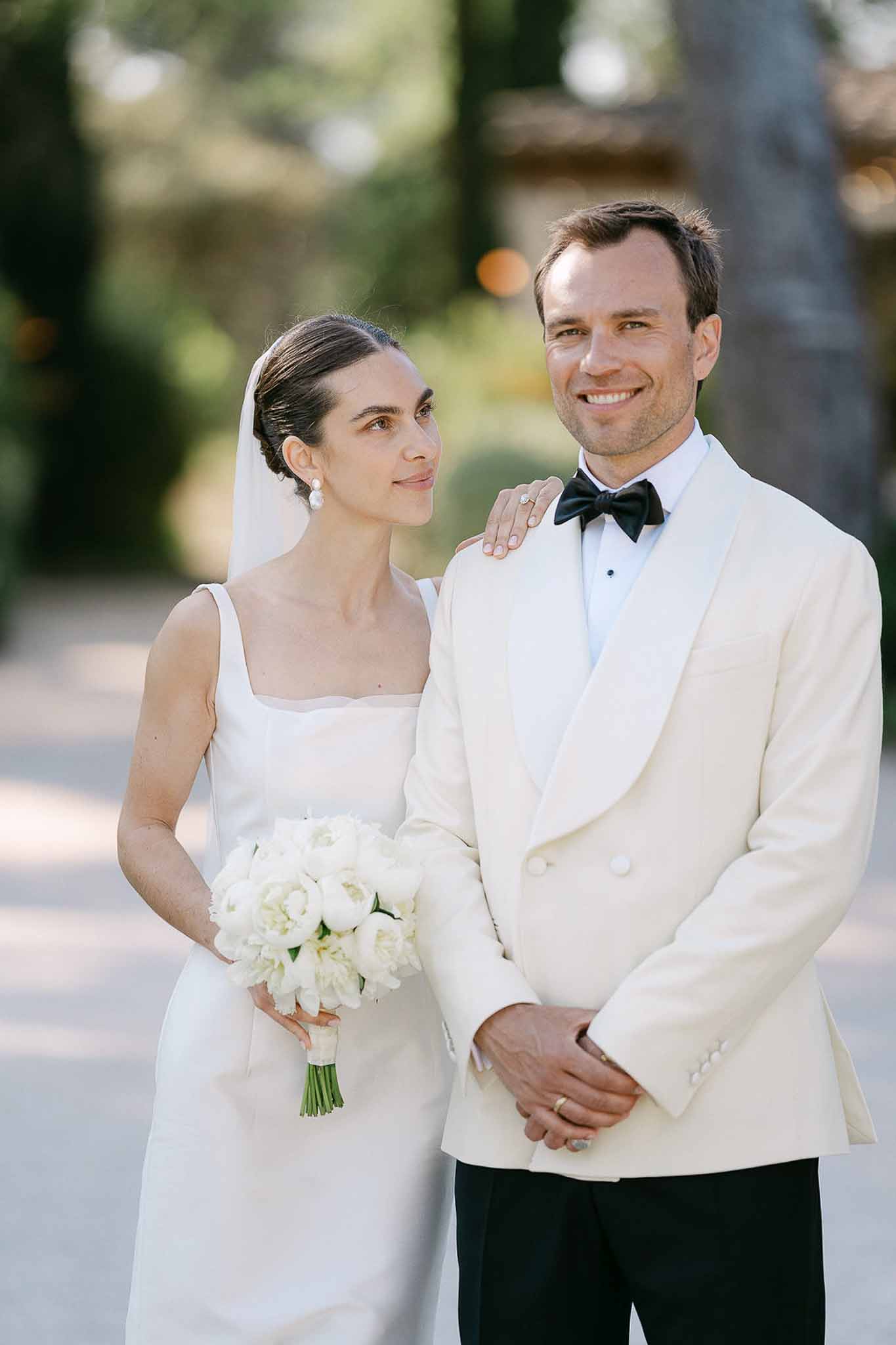 Couple portrait with bride in ivory gown holding white peony bouquet and groom in ivory dinner jacket