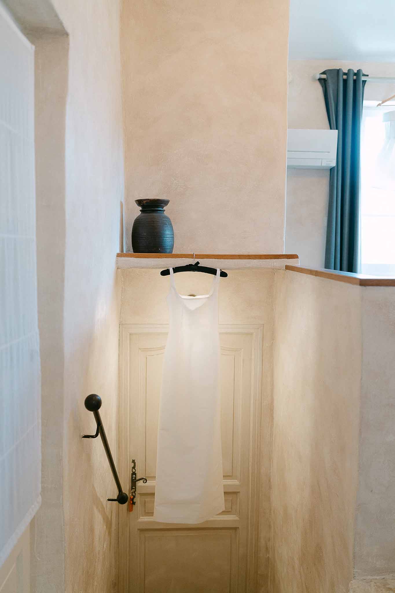 White slip-style wedding dress hanging from a wooden banister inside a French country property stairwell