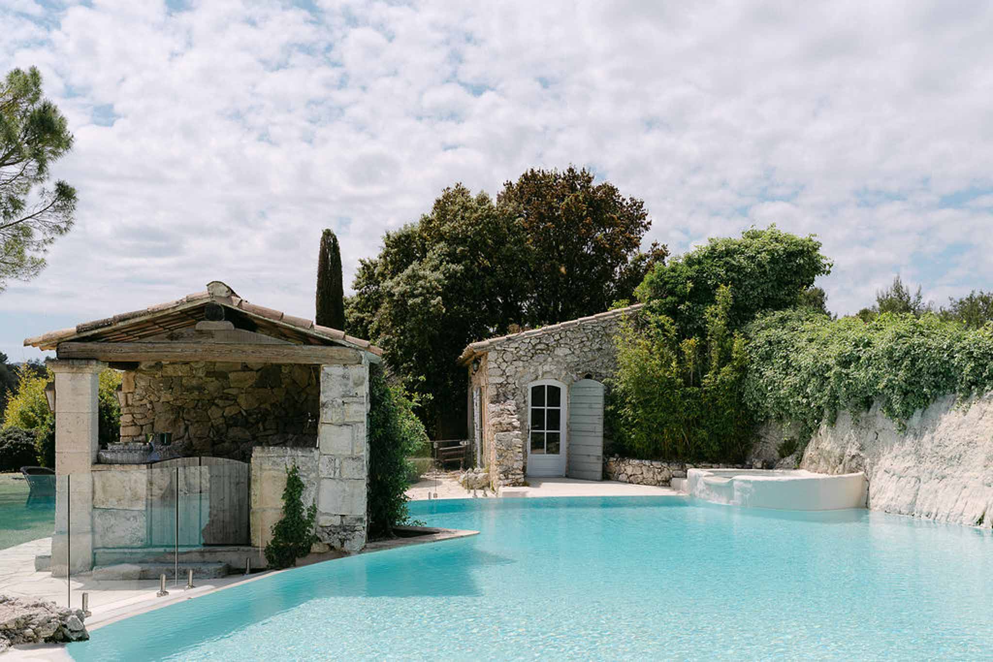 Pool area at French mas with turquoise water, stone cabana bar, and Provencal outbuilding