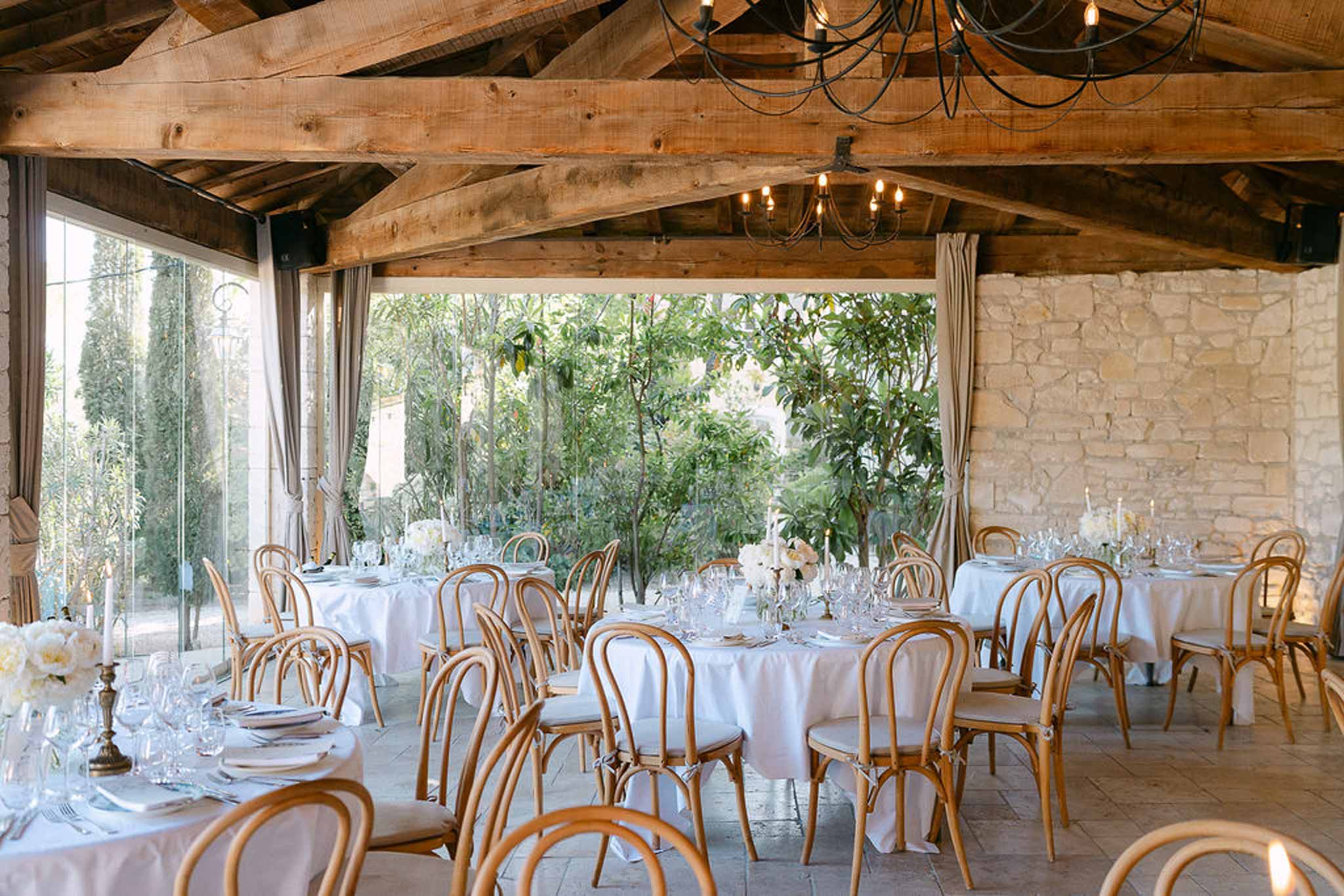 Stone-walled reception room with round white tables, brass candelabras, and bentwood chairs