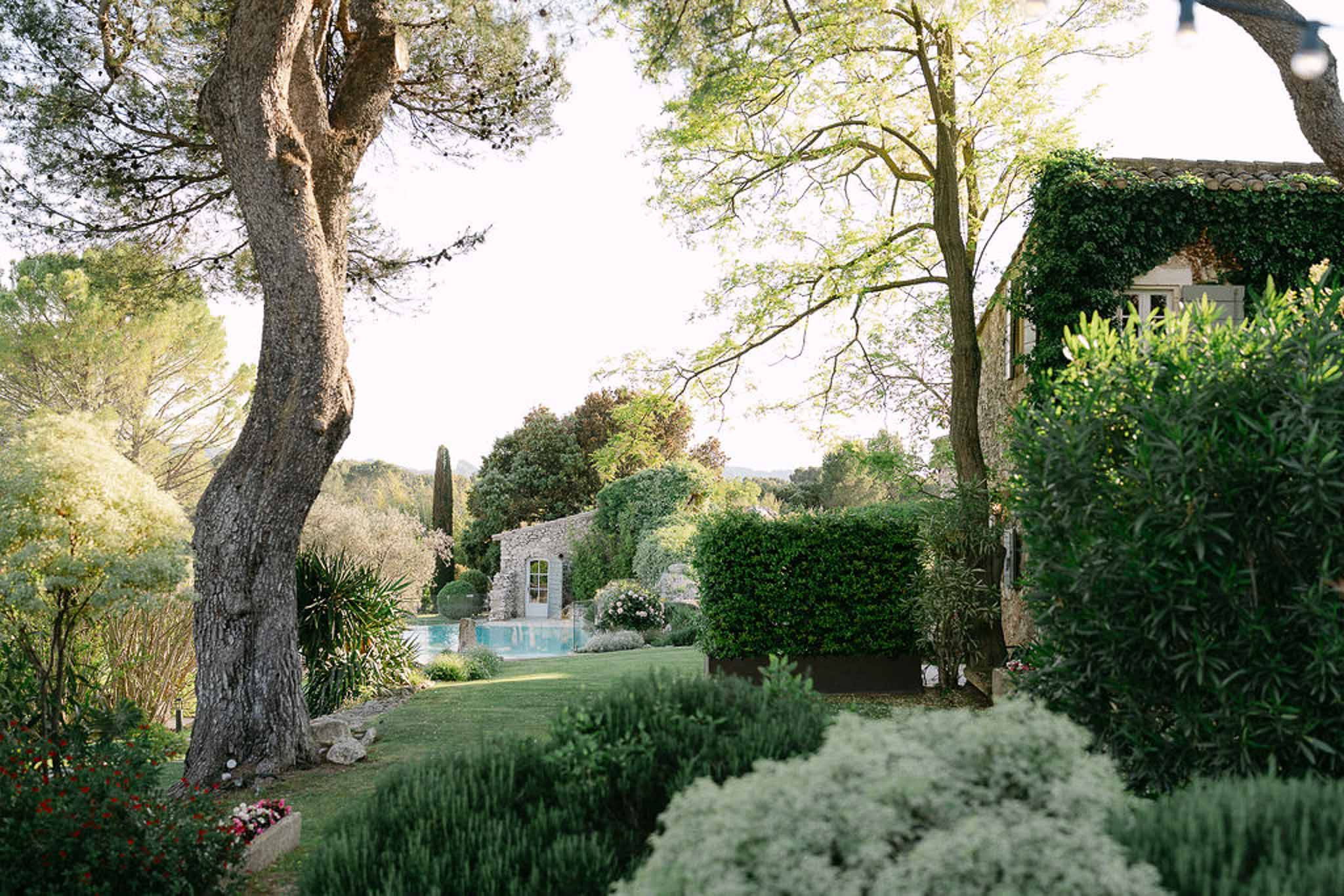 Landscaped garden with ivy-covered stone outbuilding, turquoise pool, and mature trees with string lights